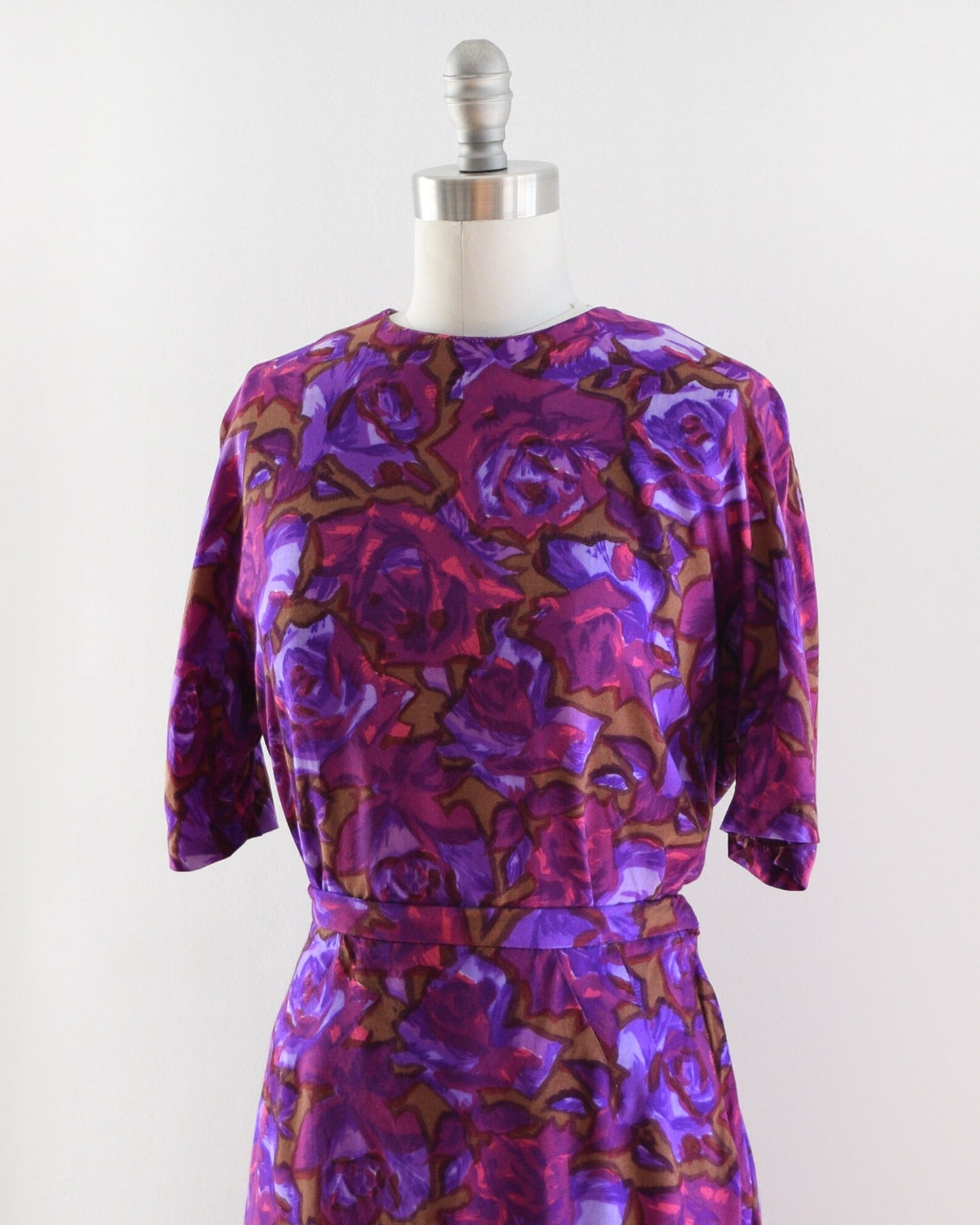 Side front view of a vintage 60s two piece top and skirt set in various shades of purple, along with bright pink, and light brown floral print.