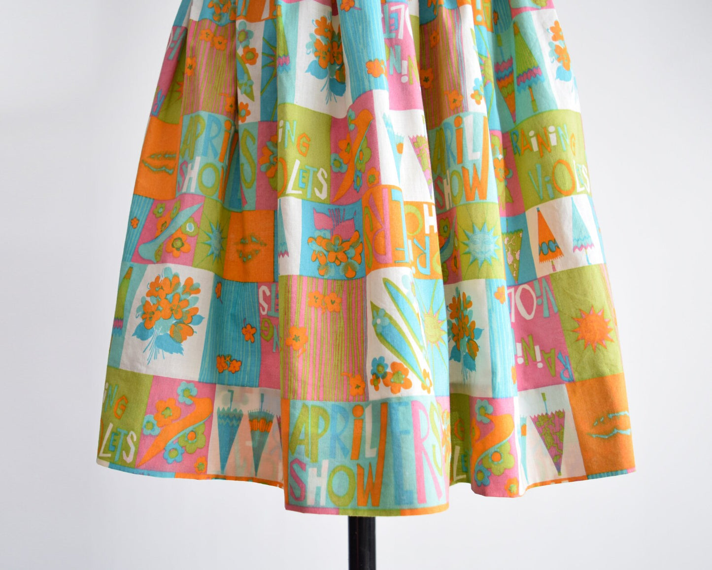 Close up print that has an April showers theme with colorful blocks of flowers, umbrellas, shoes, the sun, and the words April Showers and Raining Violets in a classic mid century print. Skirt is modeled on a dress form