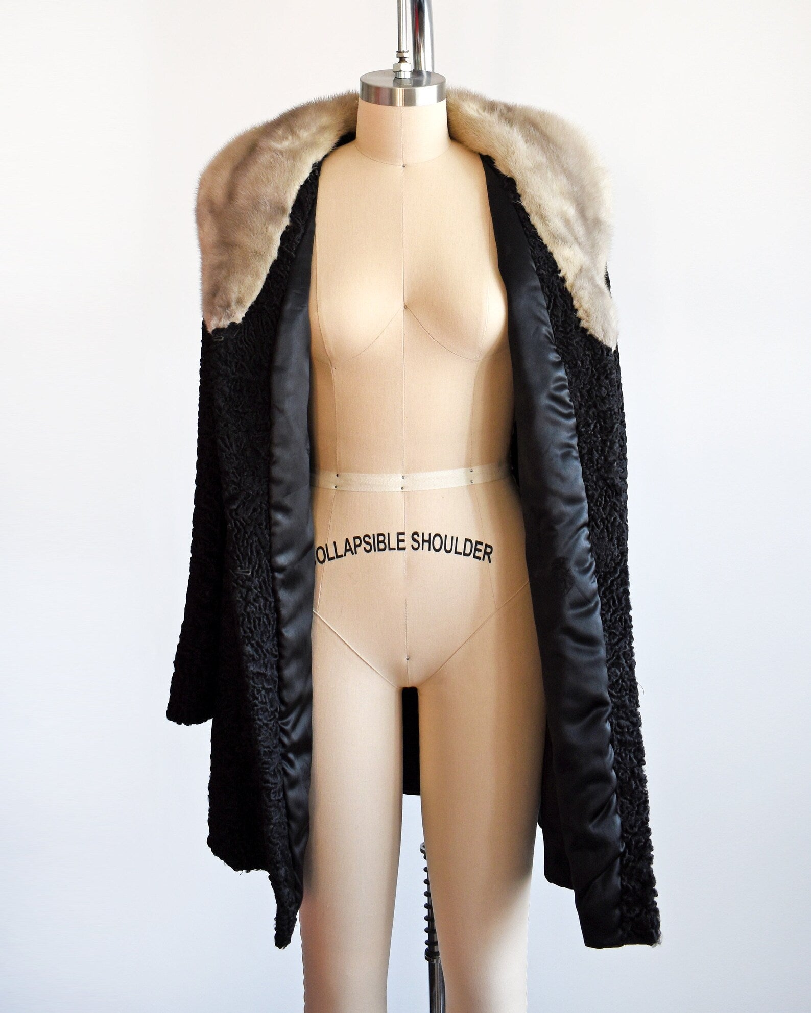 A vintage late 50s early 60s black curly Persian lamb coat that has a silver gray mink fur collar. Two hidden hook and eye closures down the front. Coat is on a dress form and is open showing the black lining