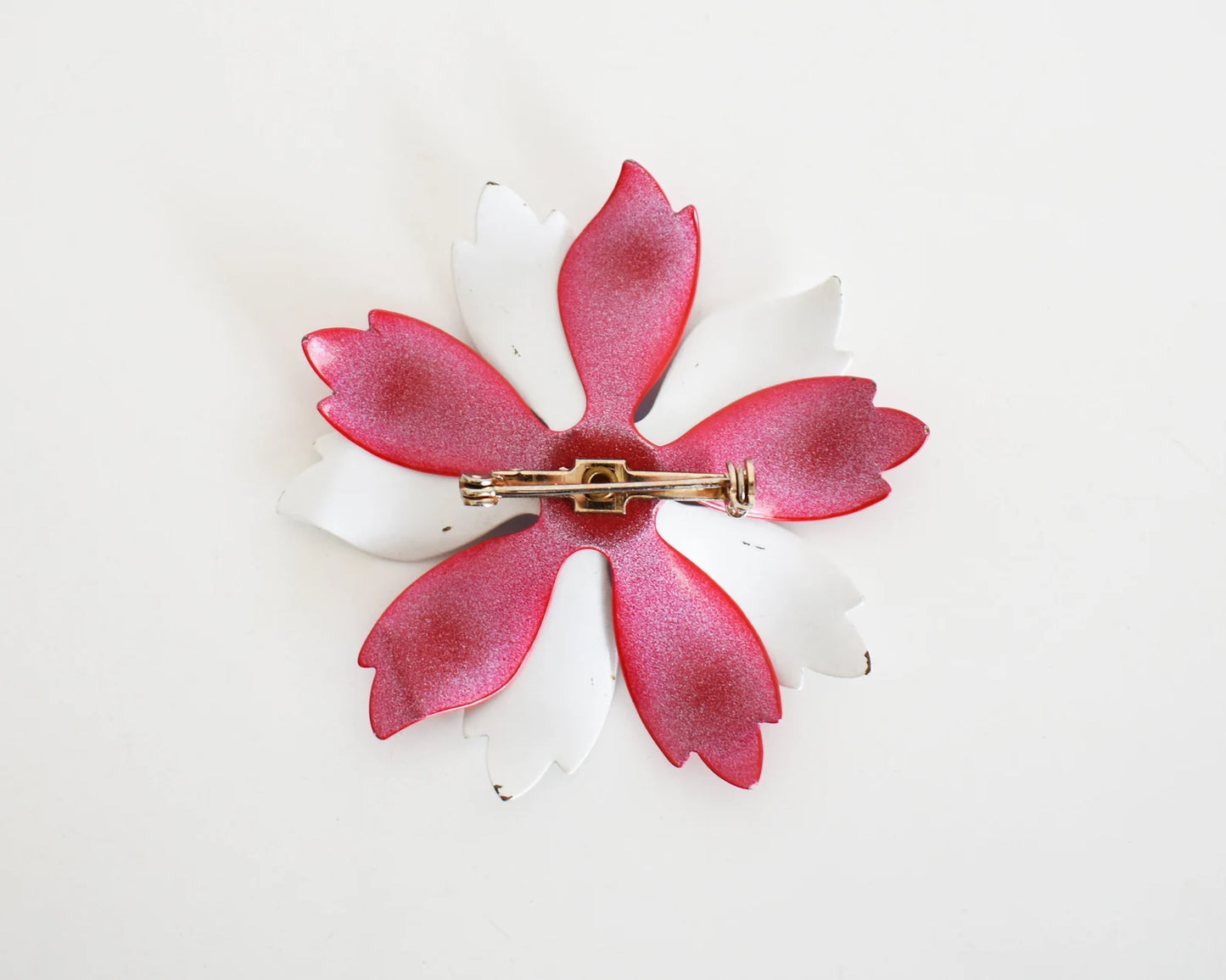 A vintage 60s mod floral brooch that has red and white petals. White and red backing with pin closure.