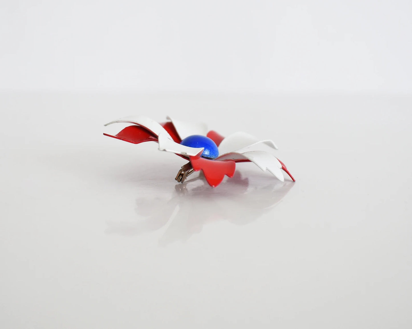 Side view of a vintage 60s mod floral brooch that has red and white petals with a blue rounded center. White and red backing with pin closure.