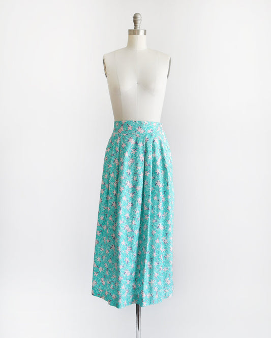 A vintage skirt that has a large turquoise colored leaf print with pink flowers with pops of purple and white buttons on the left side on a dress form.