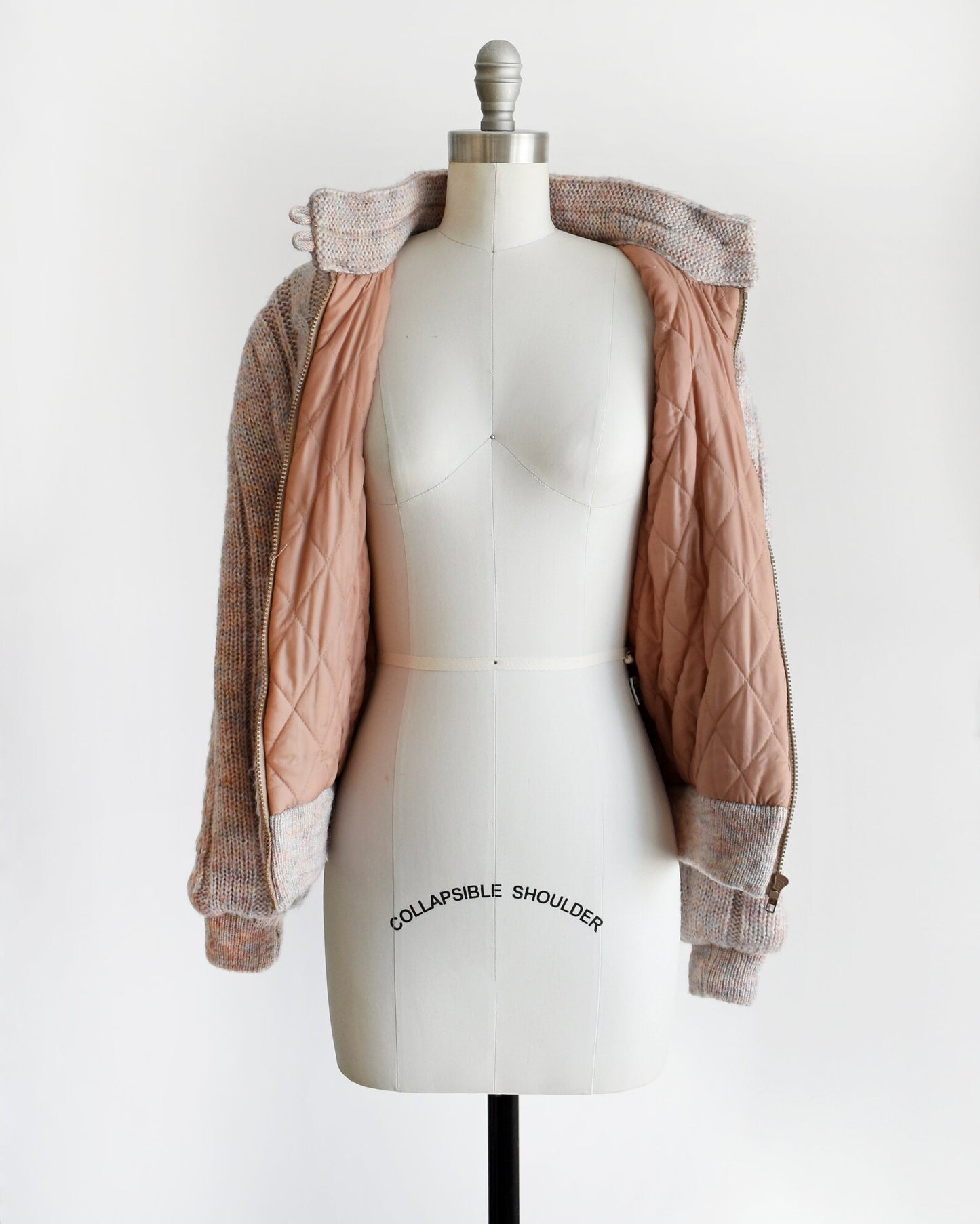 A vintage 80s light purple cable knit sweater coat on a dress form. The coat is open showing the light brown quilted lining.