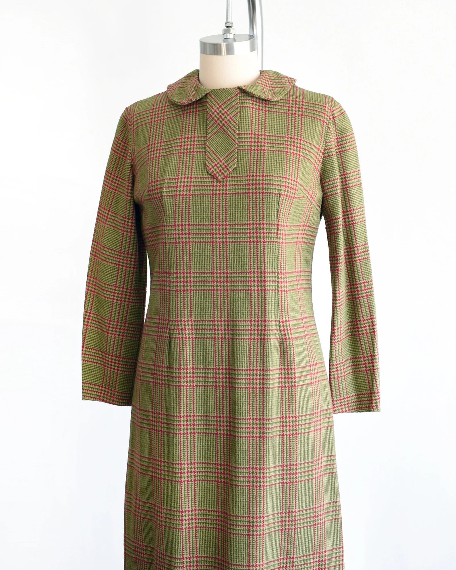 Side front view of a vintage 60s green and pink plaid wool dress with Peter Pan style collar and long sleeves. The dress is modeled on a dress form.