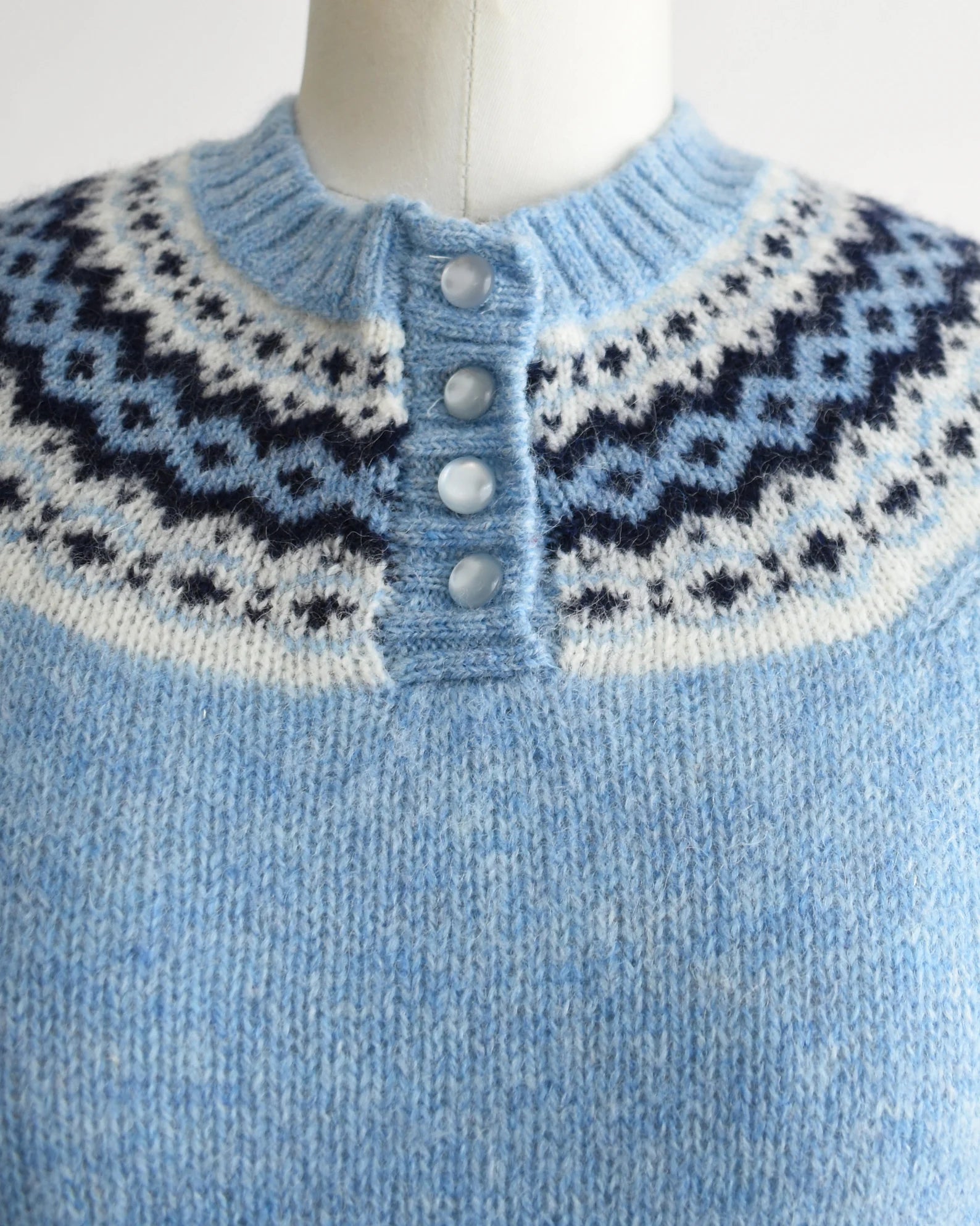 Close up of the fair isle pattern around the collar and 4 buttons down the front. The sweater is modeled on a dress form.