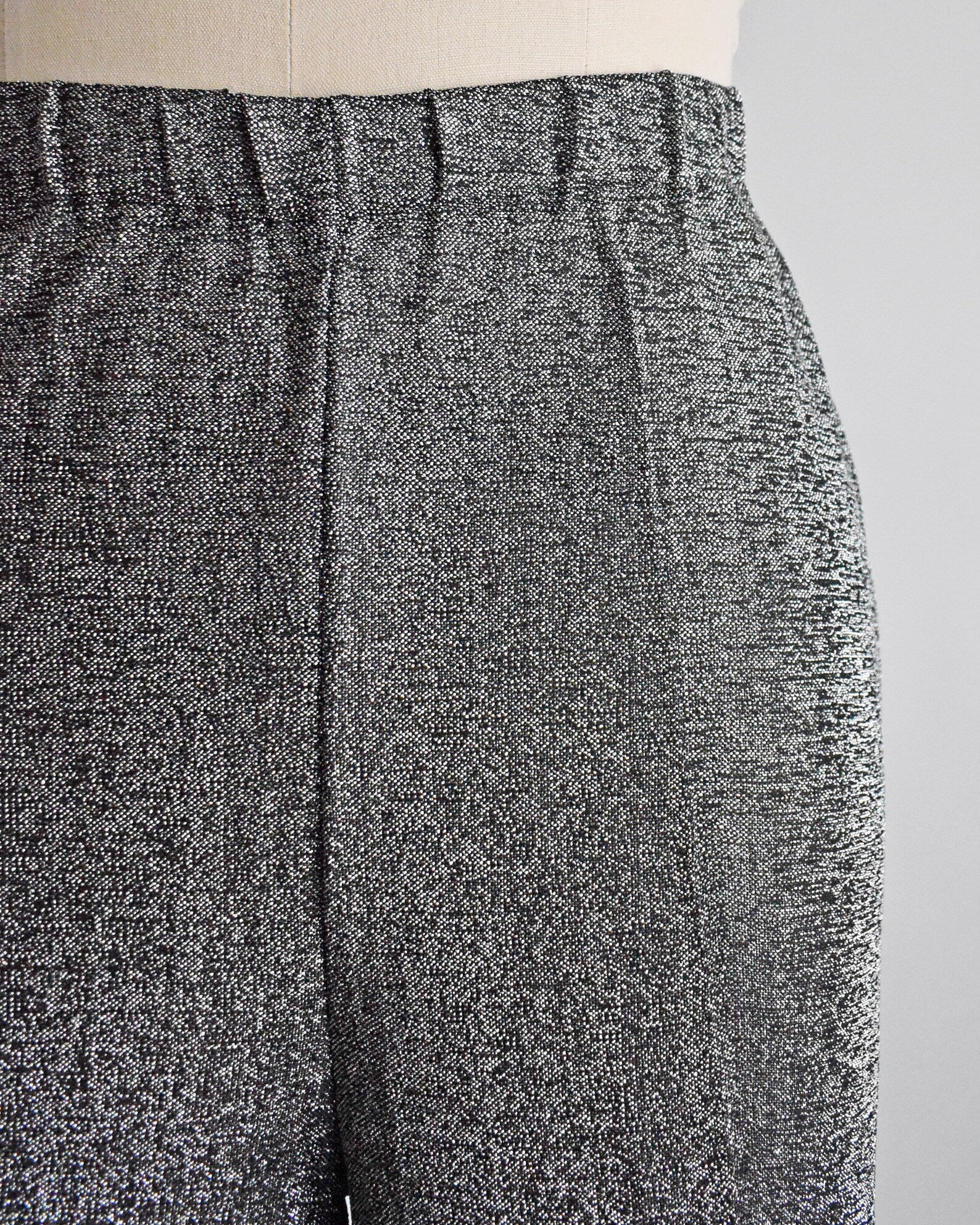 Close up of the waist and hips of a vintage pair of 70s silver and black metallic pants on a dress form.