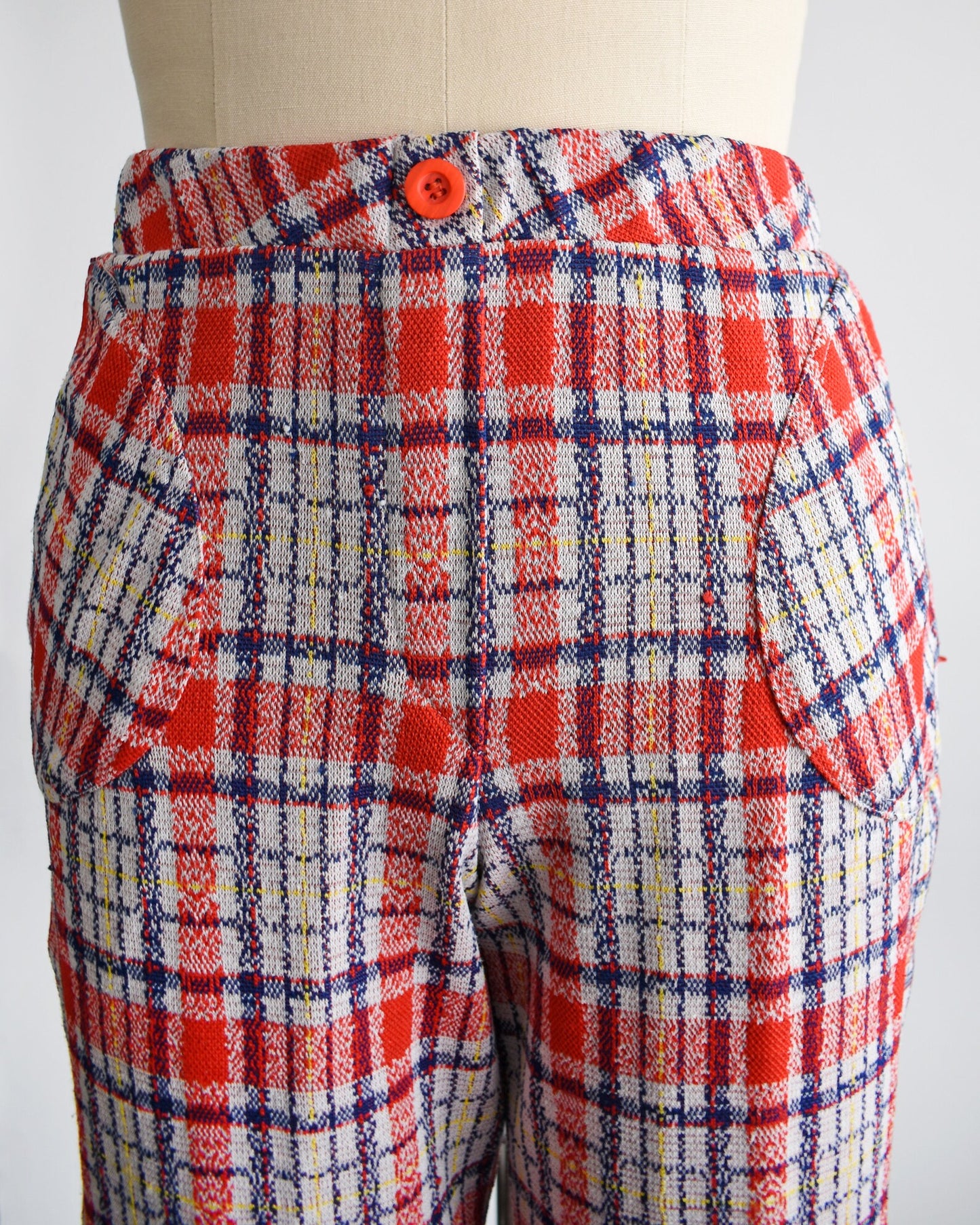 Close up of the upper part of the pants that shows a decorative red button at the center of the waist, the plaid, and the rounded hip pockets.