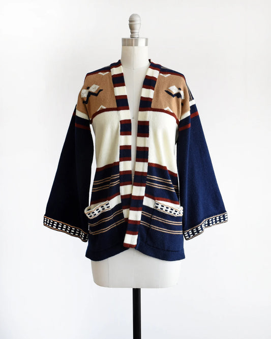 A vintage 70s navy blue, tan, reddish brown, and white striped bell sleeve open cardigan on a dress form.