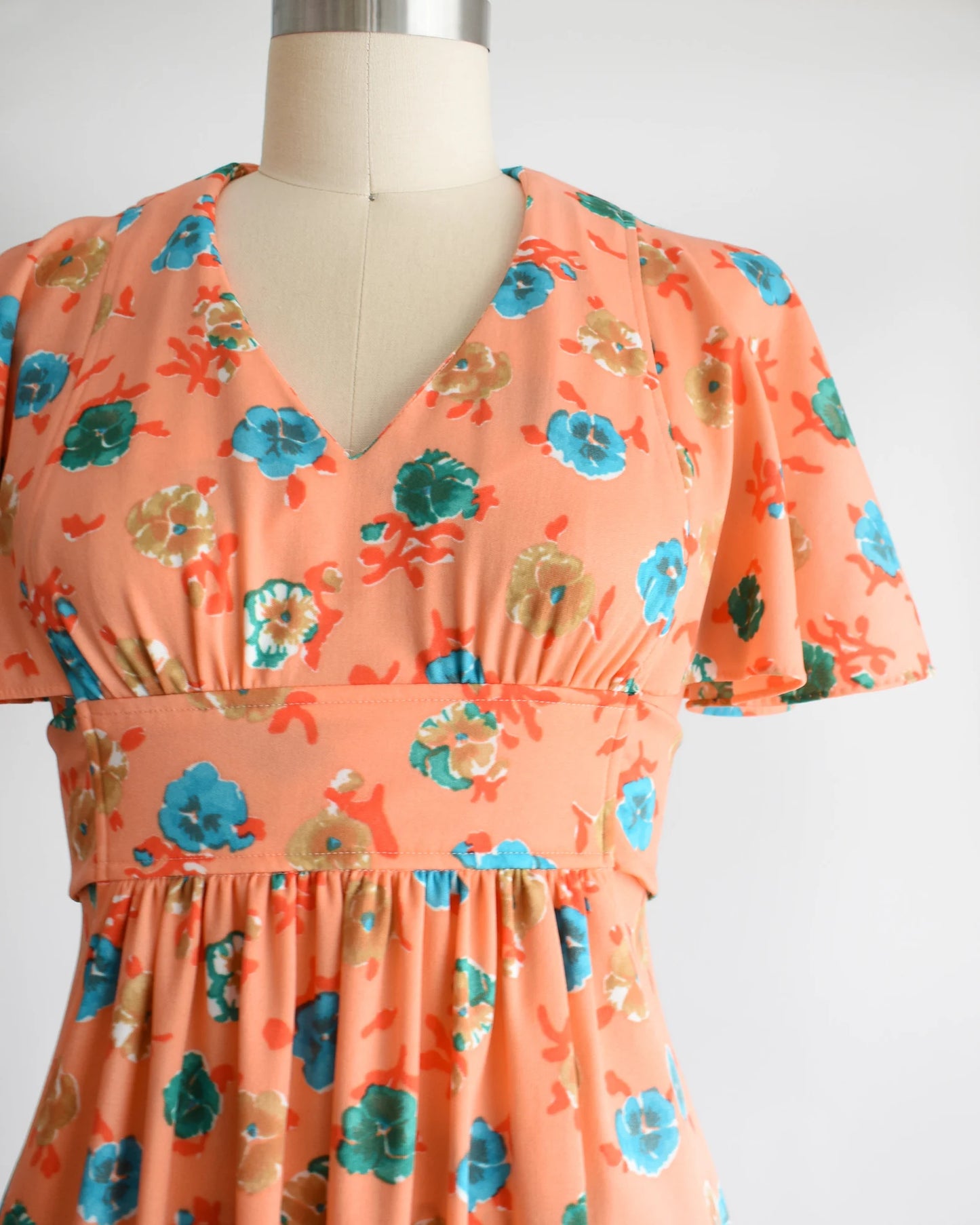 Close up of the floral print, v-neckline, flutter sleeves, and empire waist.