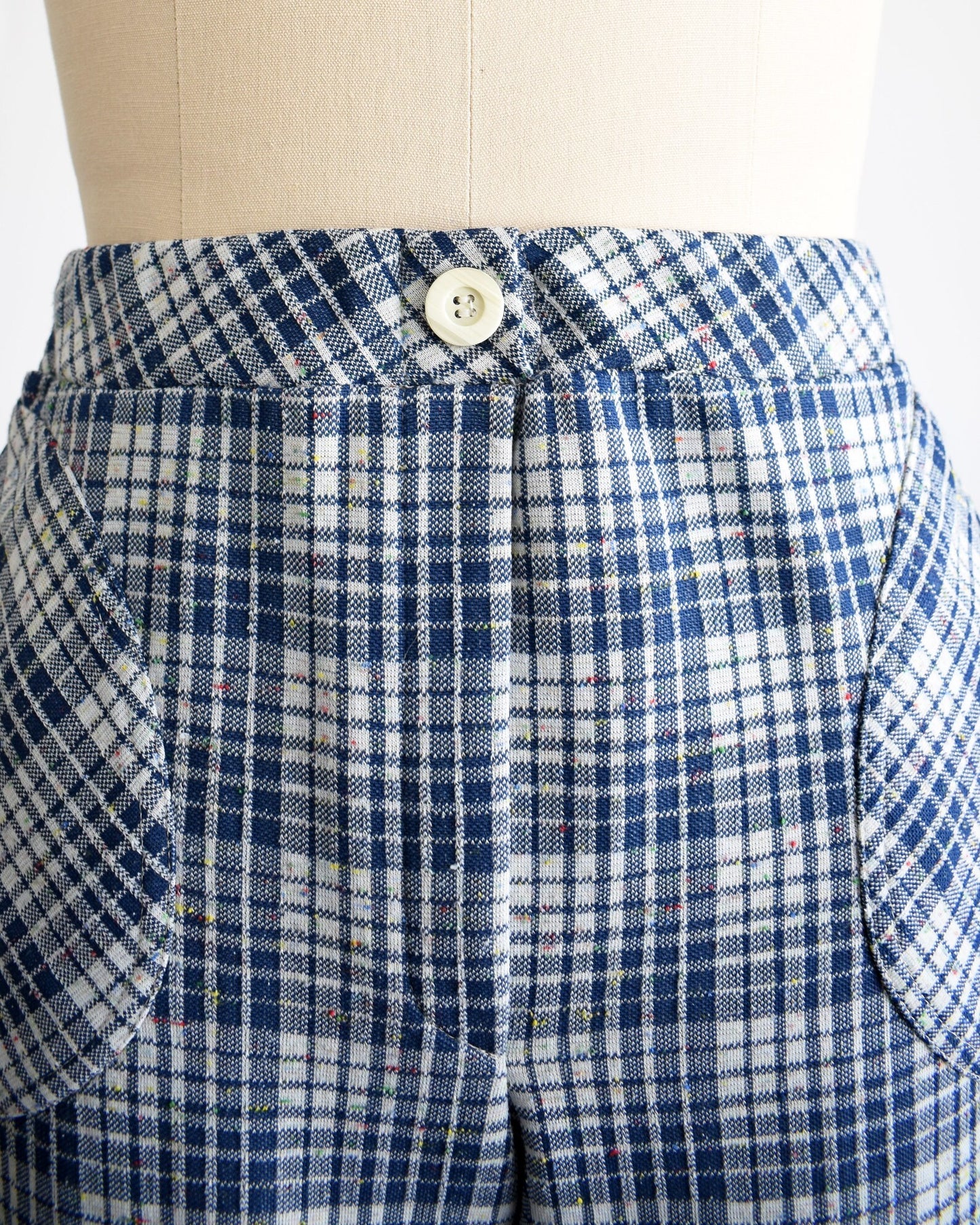 Close up of the upper part of the pants that shows a decorative white button at the center of the waist, the plaid, and the rounded hip pockets.