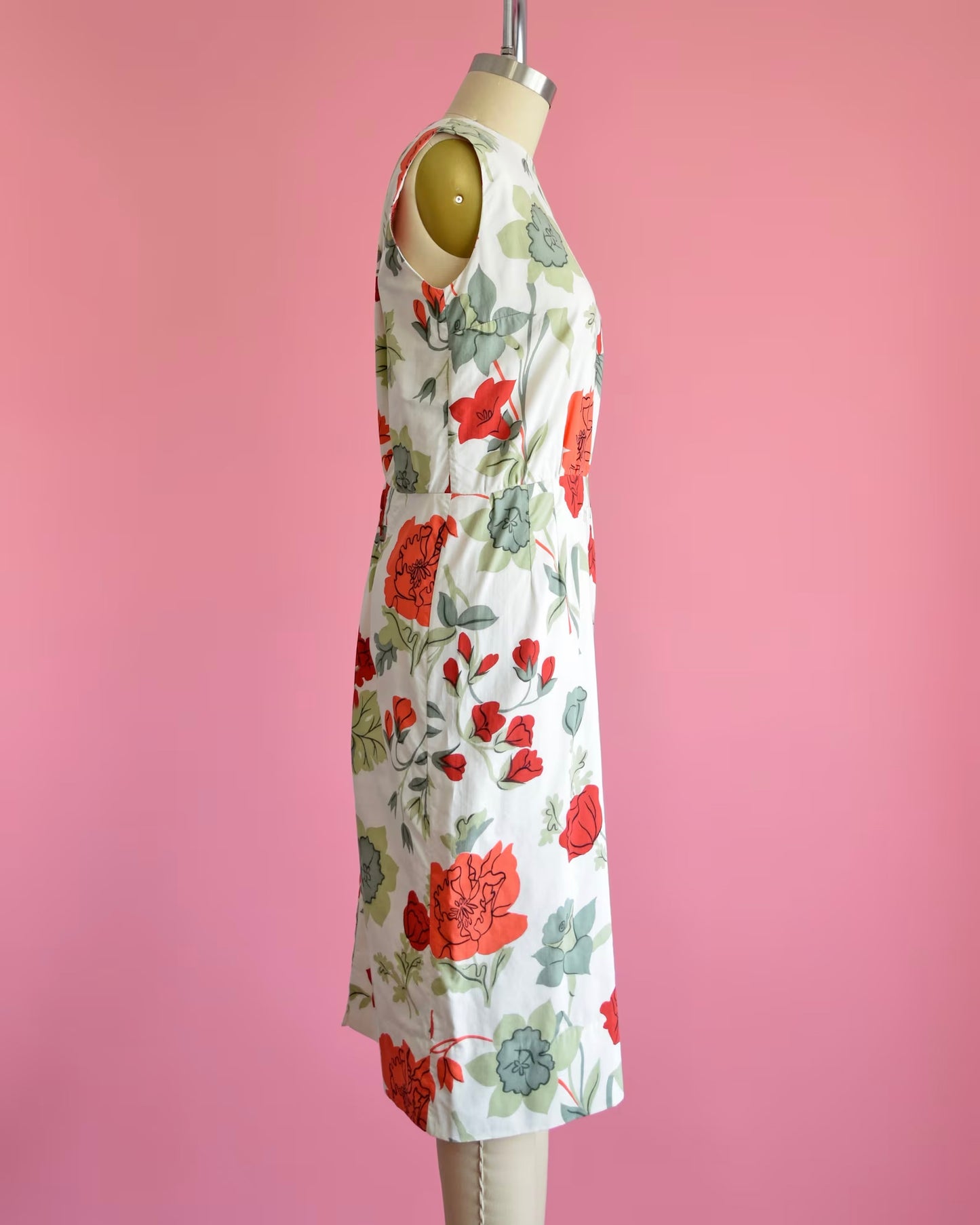 Side view of a vintage 60s white dress with a large red and green floral print on a dress form.