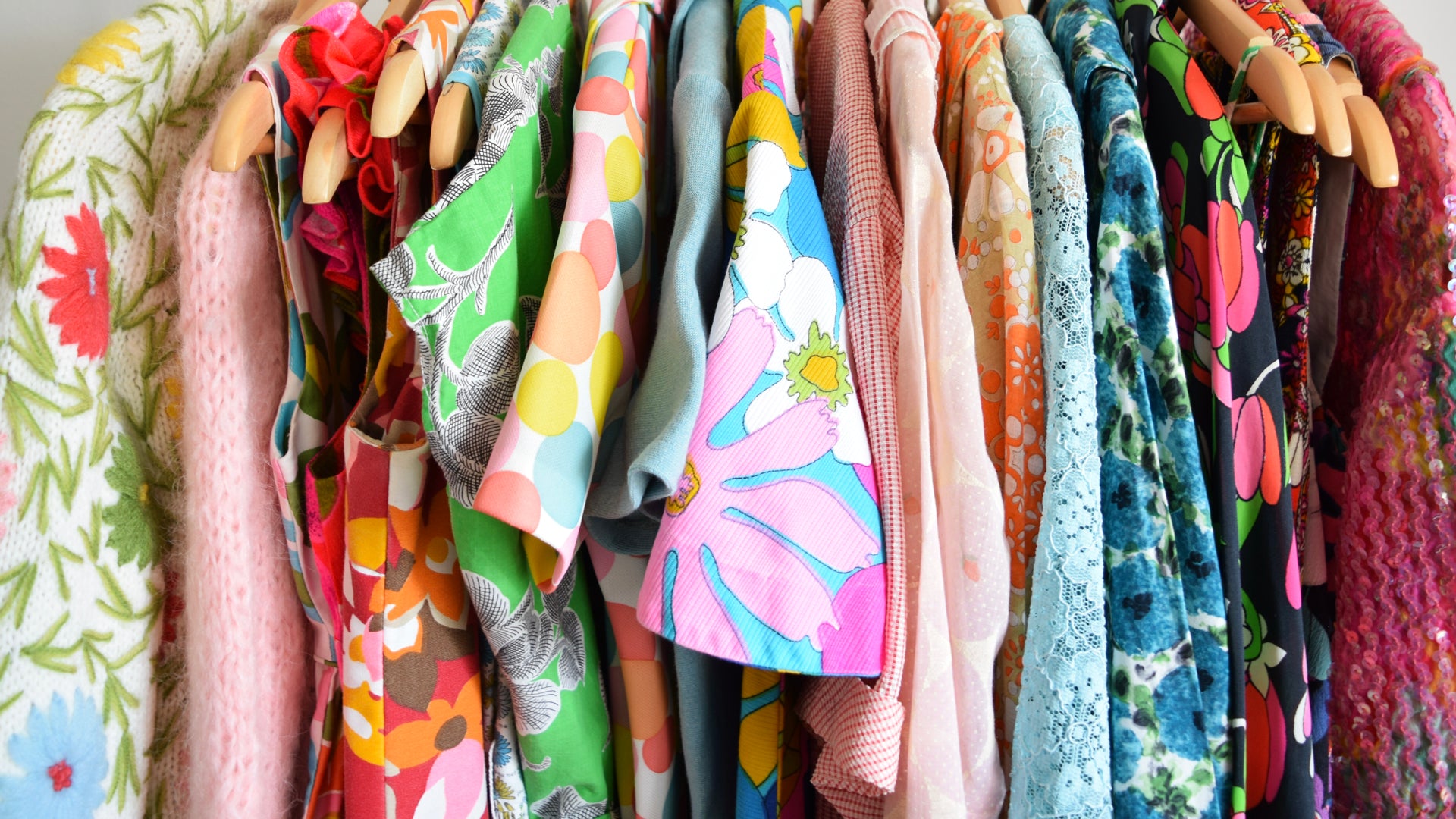 A close up of a row of colorful vintage clothing in all sorts of patterns on wooden hangers