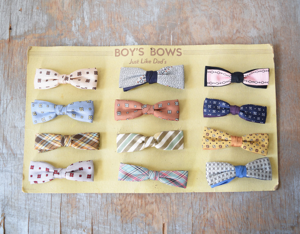 12 different types of clip on bow ties on all sorts of colors and prints on a yellow board