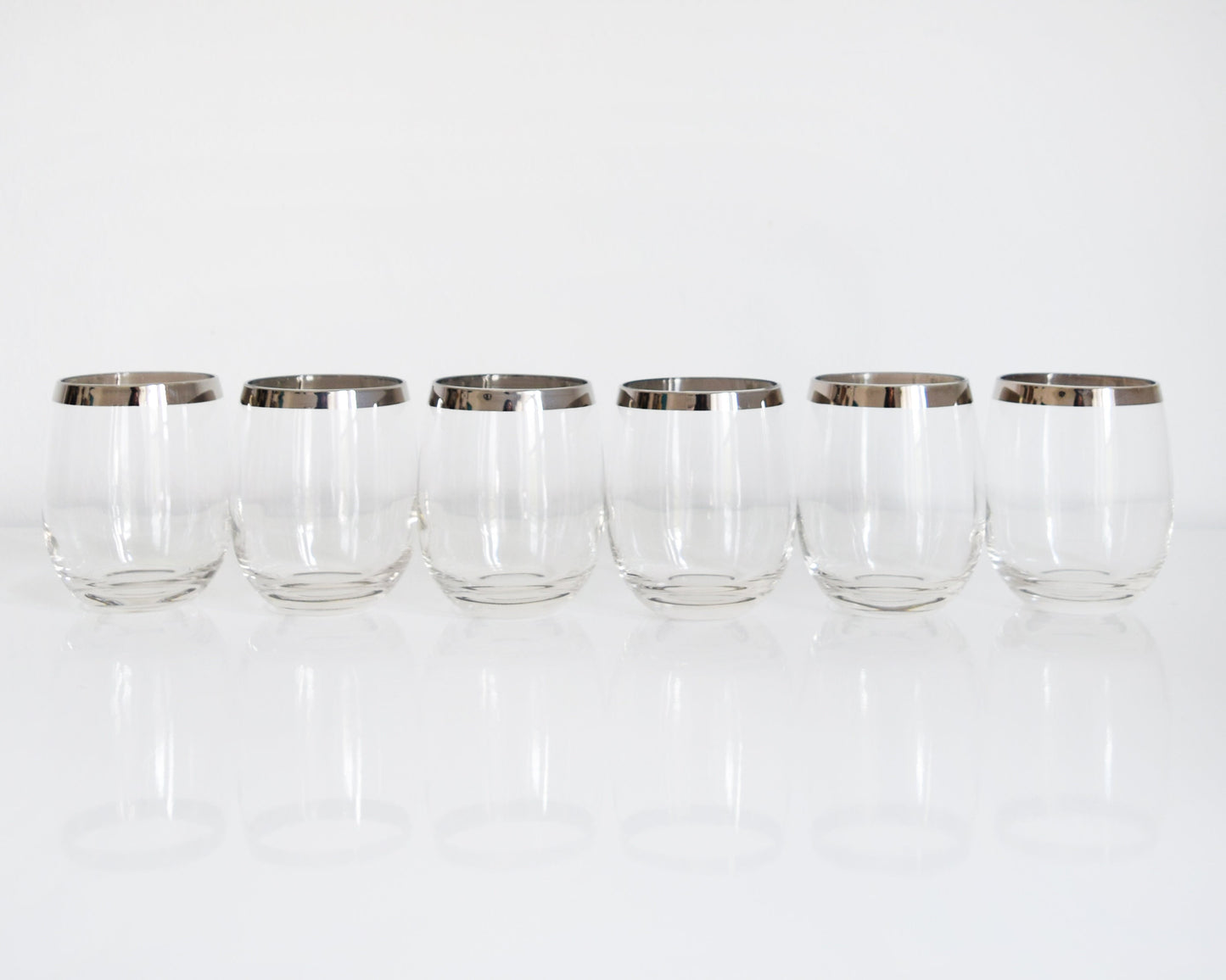 A row of 6 vintage 60s sliver rim tumblers that have an elongated roly poly shape