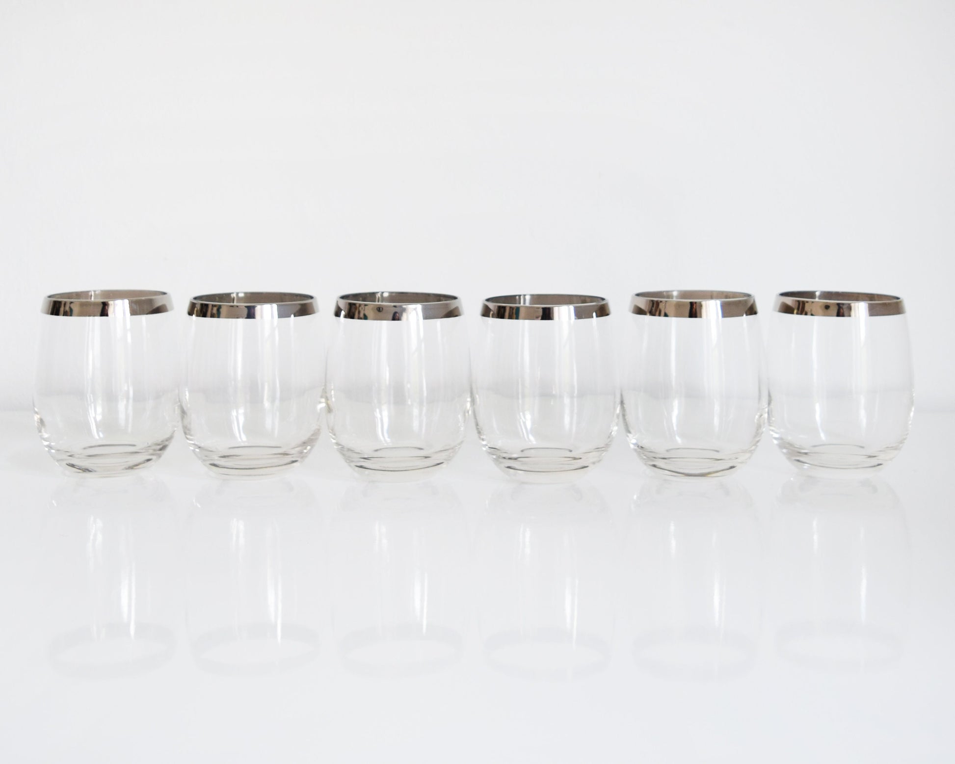A row of 6 vintage 60s sliver rim tumblers that have an elongated roly poly shape