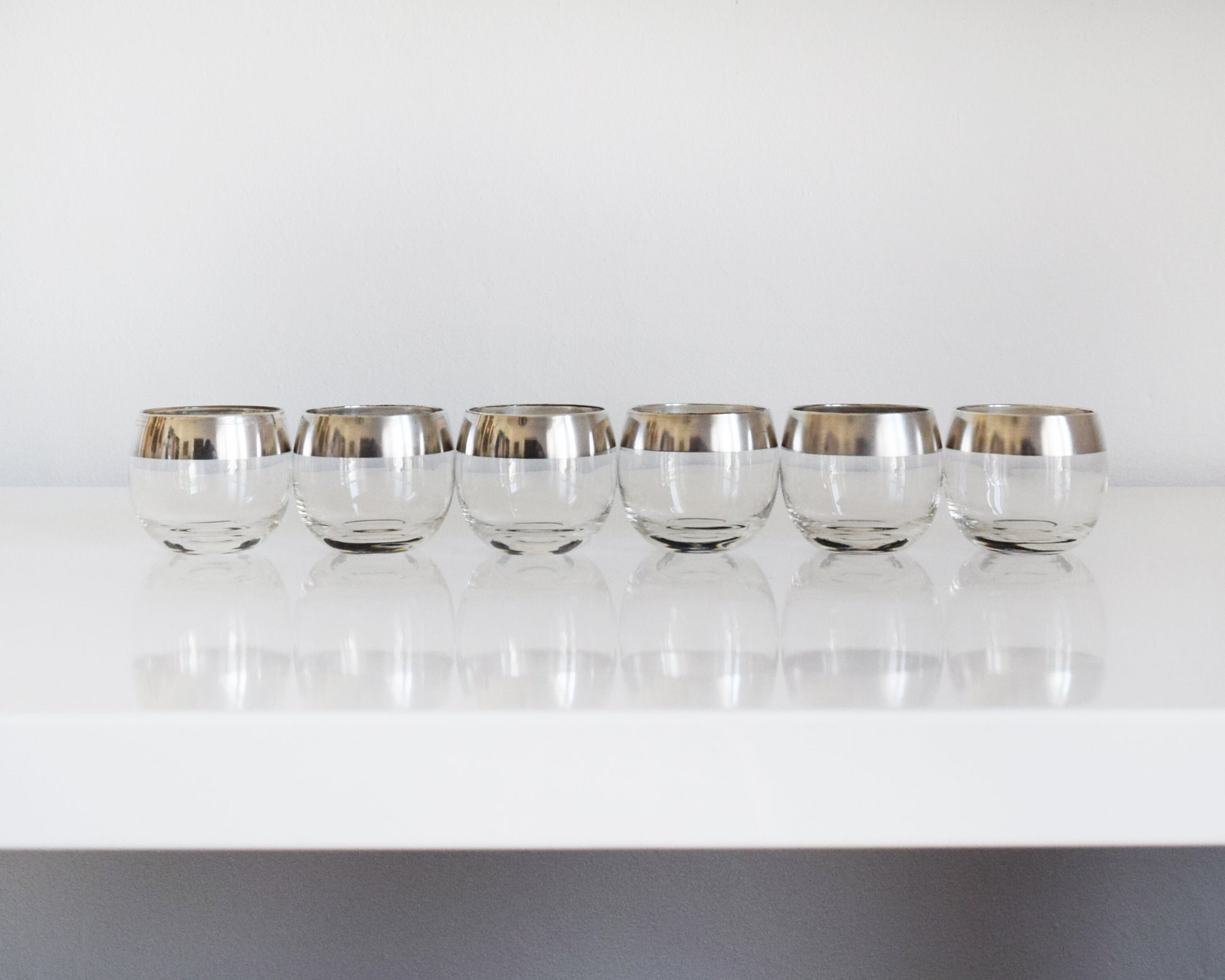 Six silver rimmed rounded roly poly glasses in a row