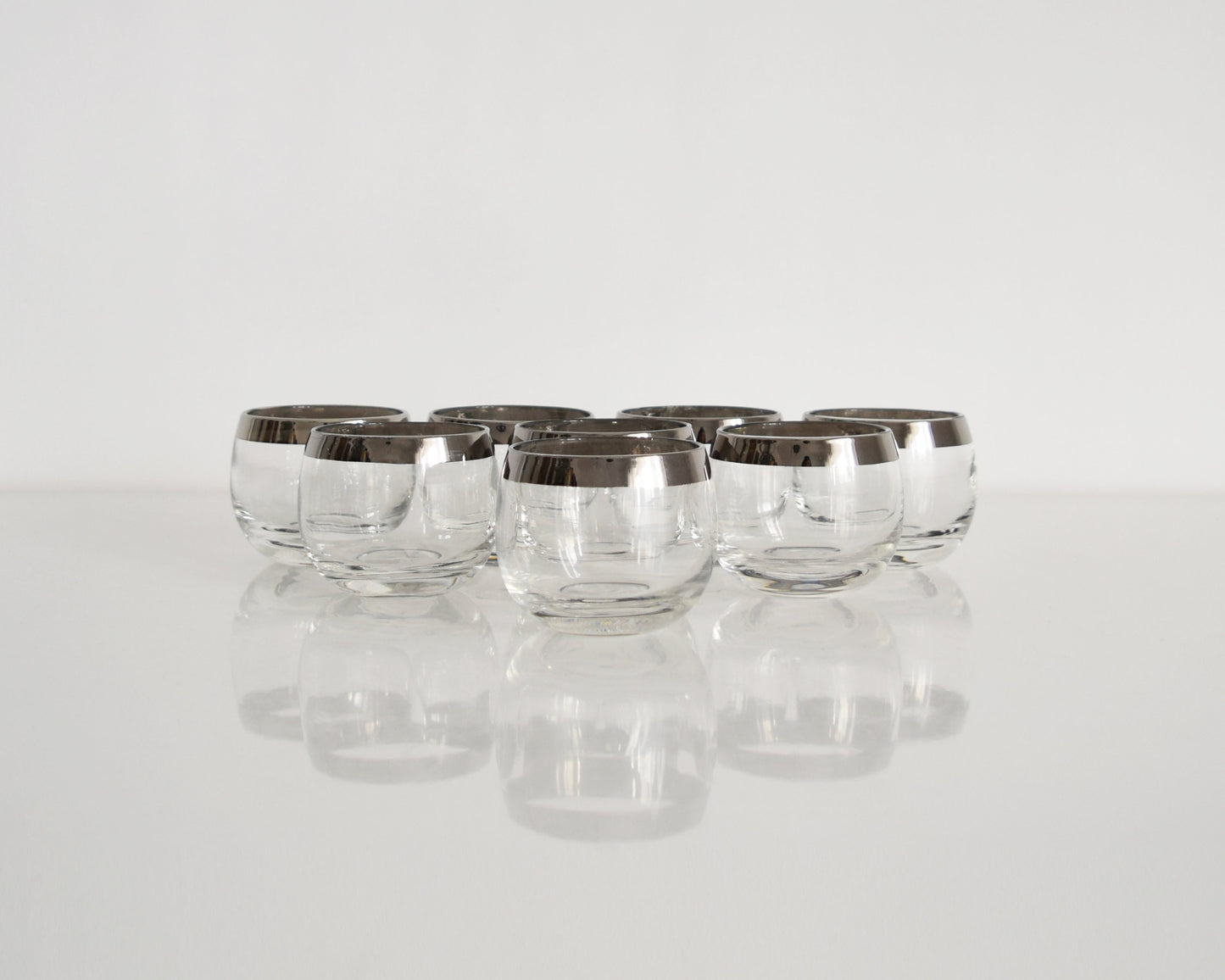 front view of eight silver rim roly poly glasses that are round with flat bottoms on a table