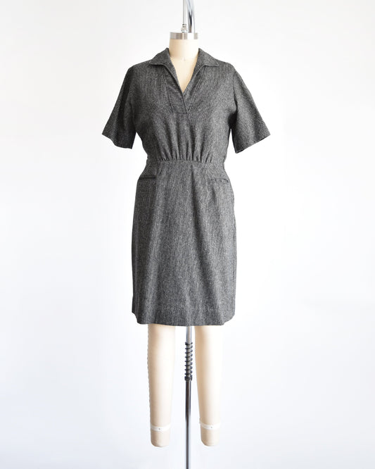 A 1950s vintage wool dress that is black and white striped with a v-neck collared neckline, short sleeves, fitted waist, and two front pockets below the waist. Dress is on a dress form