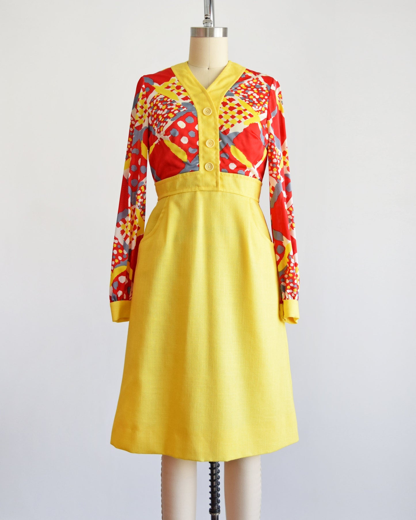 A vintage 70s dress that has a red and yellow multicolor geometric print bodice, a-line style skirt with two front pockets