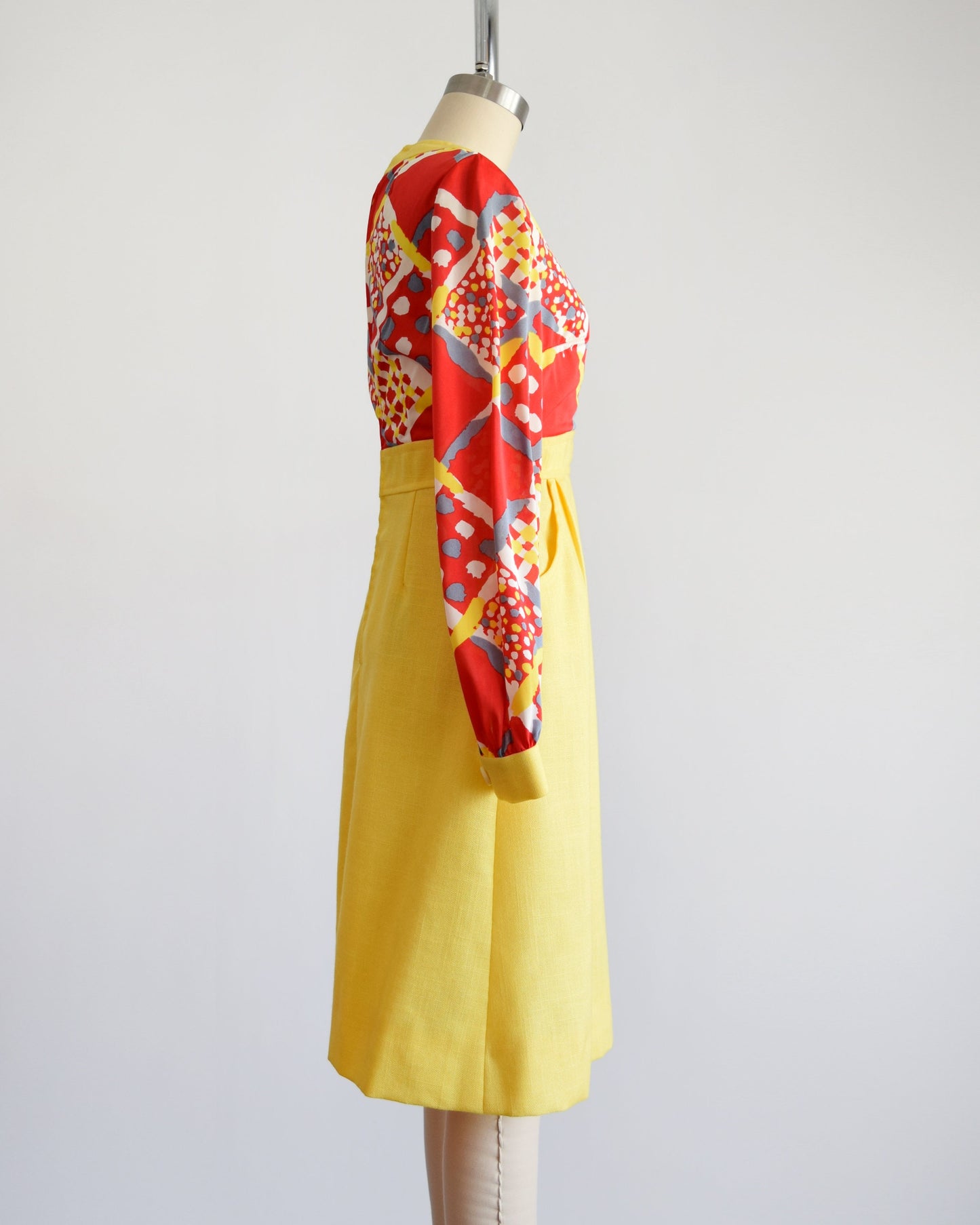 Side view of a vintage 70s dress that has a red and yellow multicolor geometric print bodice, a-line style skirt with pockets