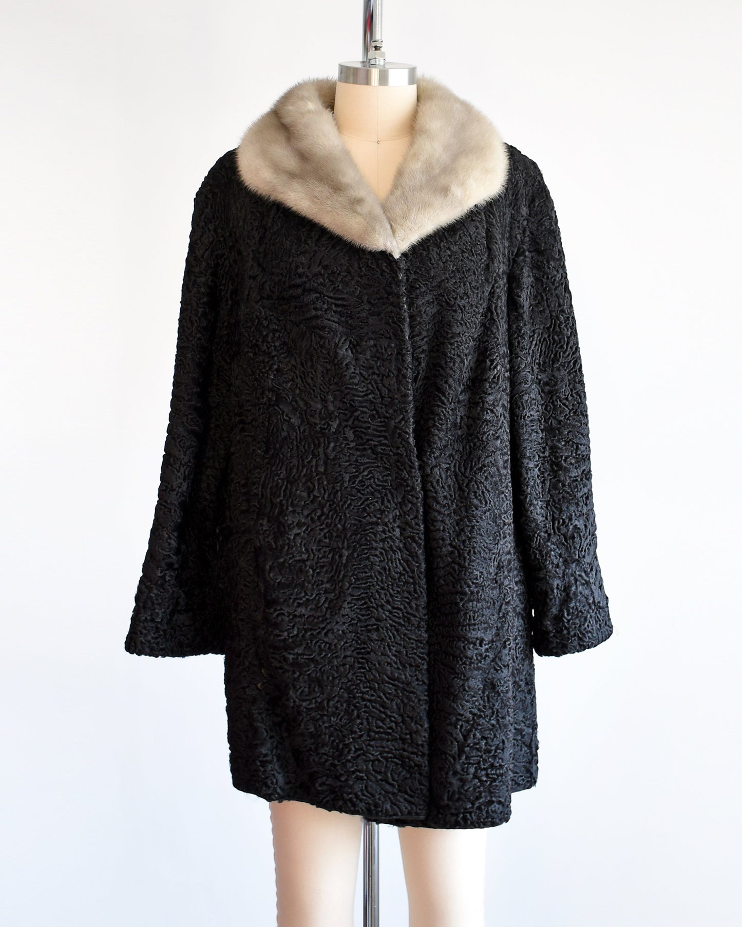 A vintage late 50s early 60s black curly Persian lamb coat that has a silver gray mink fur collar. Two hidden hook and eye closures down the front. Coat is on a dress form.