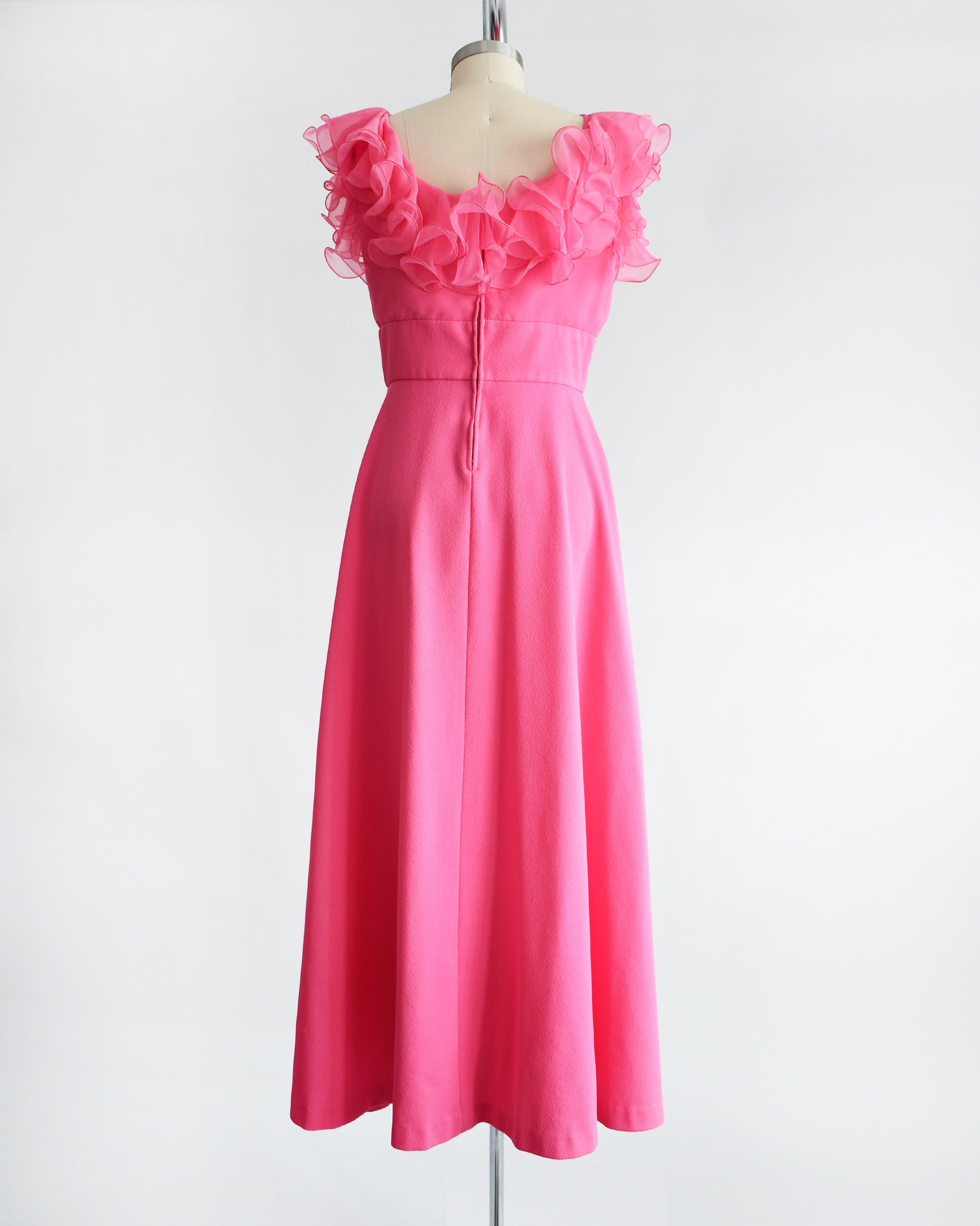 Back view of a vintage 1970s hot pink maxi dress that has a ruffled neckline and a zipper up the back