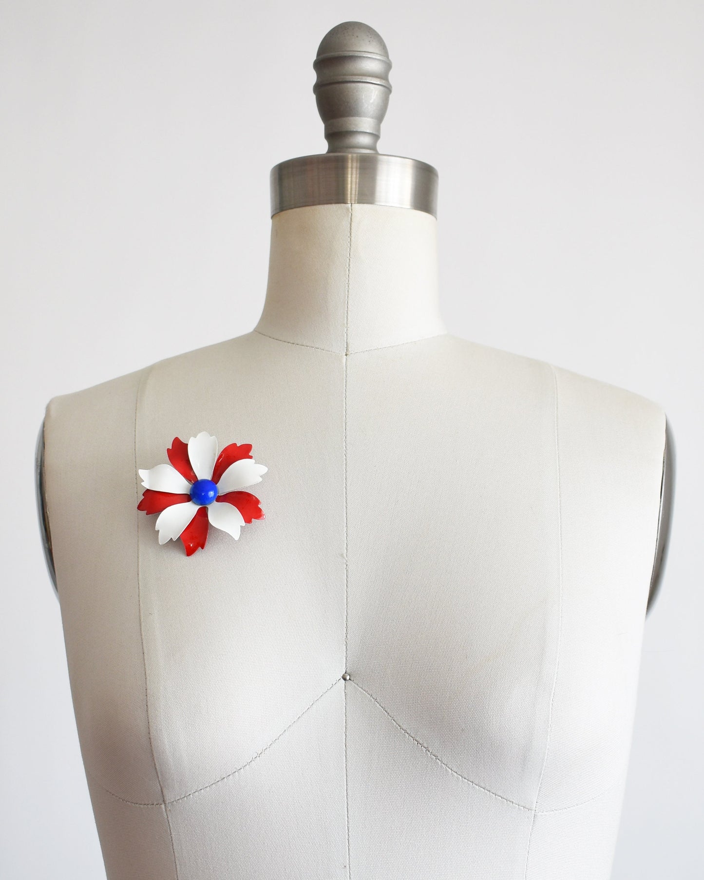 A vintage 60s mod floral brooch that has red and white petals with a blue rounded center. The pink is on a dress form