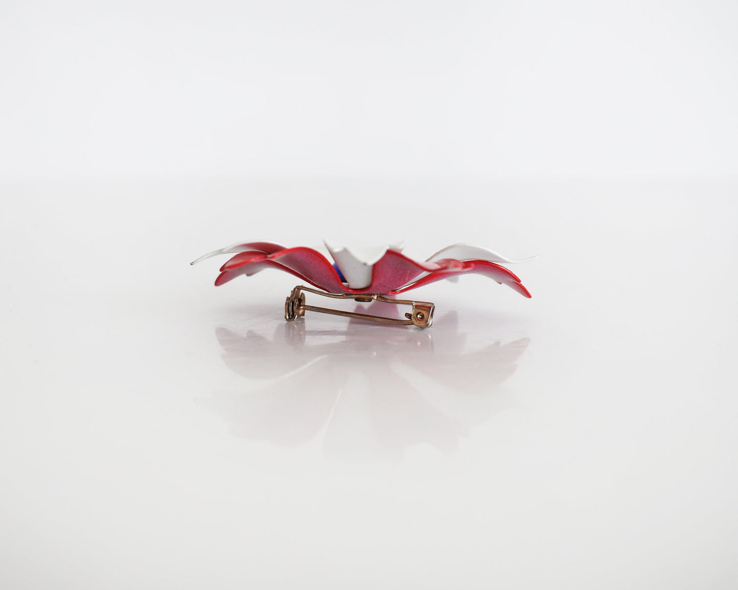 Side view of a vintage 60s mod floral brooch that has red and white petals with a blue rounded center. Pin closure.