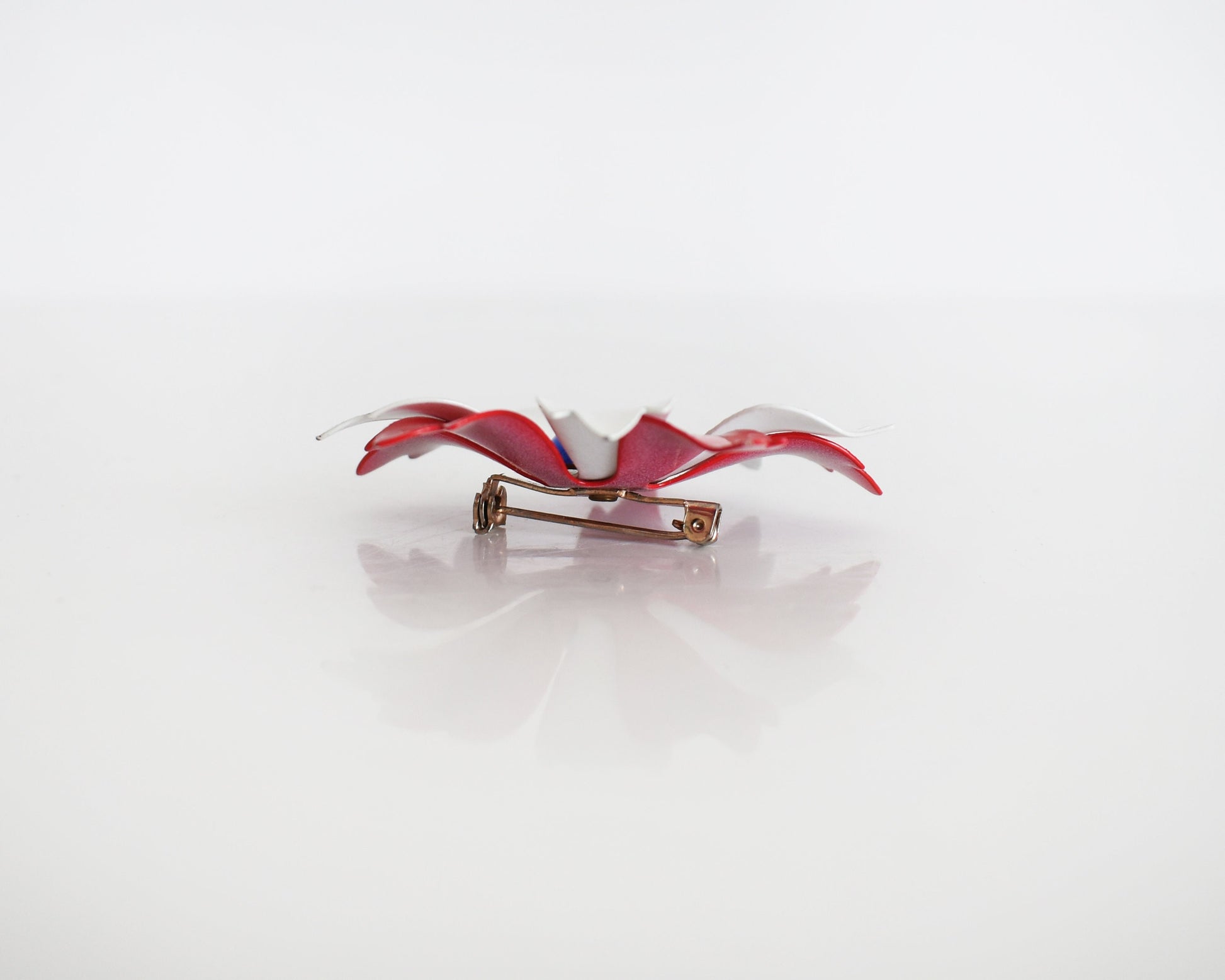 Side view of a vintage 60s mod floral brooch that has red and white petals with a blue rounded center. Pin closure.