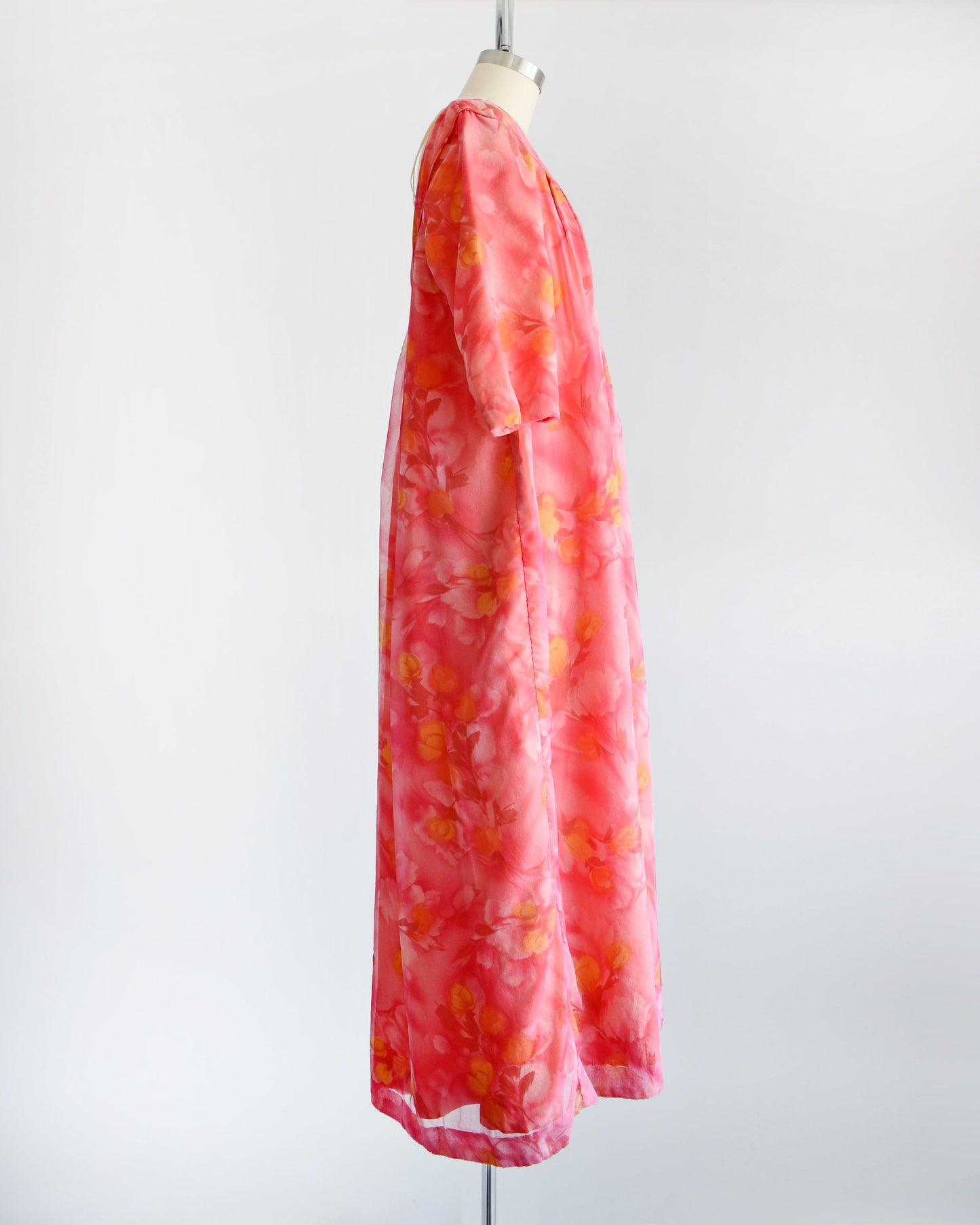 Side view of a vintage floral maxi dress with pinks, dark red, orange, and yellow floral print. The dress has half sleeves and is on a dress form.