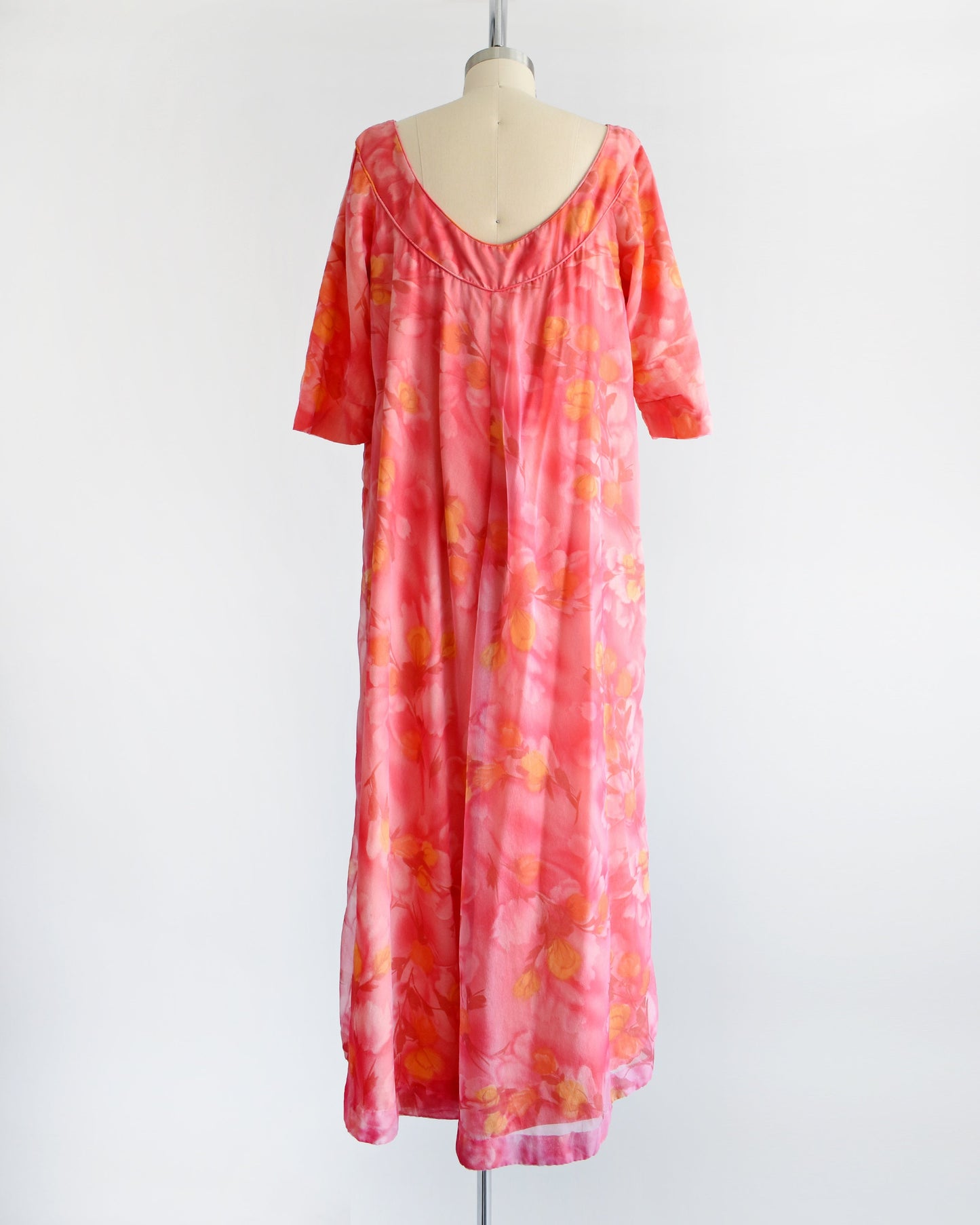 Back view of a vintage floral maxi dress with pinks, dark red, orange, and yellow floral print. The dress has half sleeves and is on a dress form.