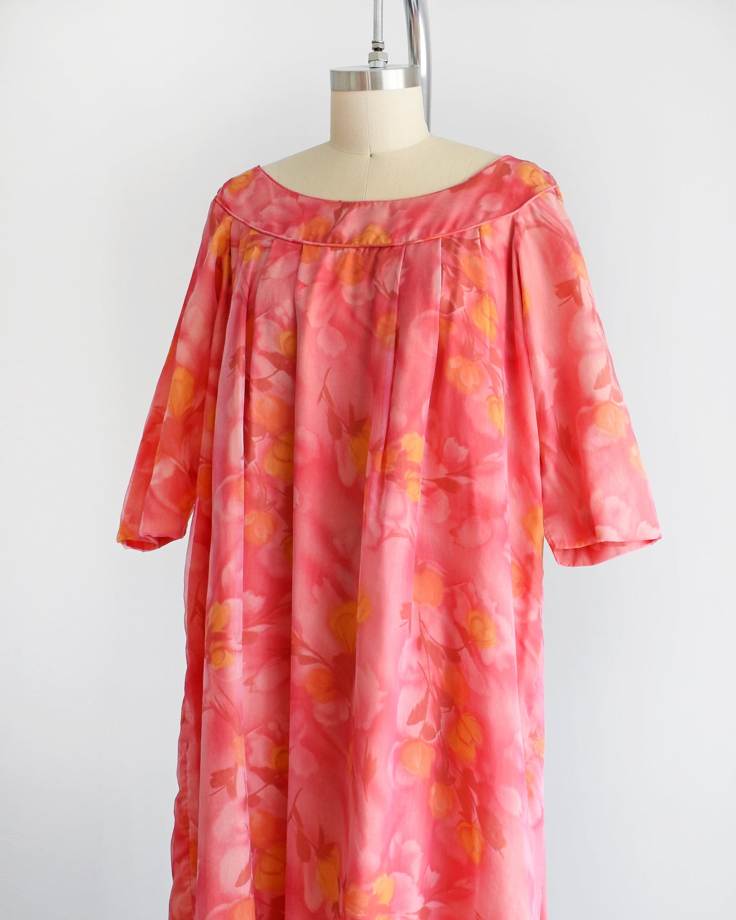 Side front view of a vintage floral maxi dress with pinks, dark red, orange, and yellow floral print. The dress has half sleeves and is on a dress form.