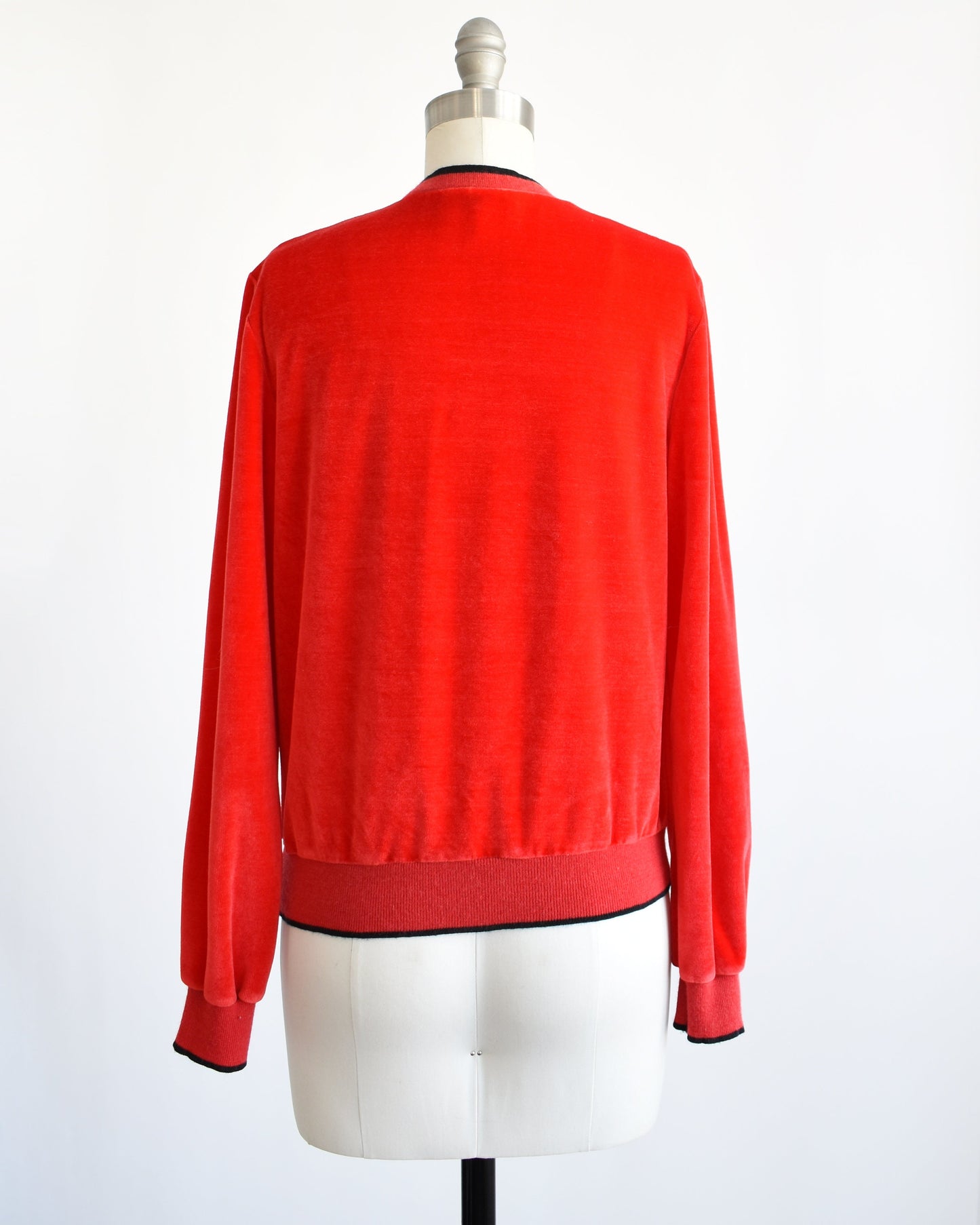 Back view of a vintage 70s red velour top with black trim along the neckline, cuffs, and hem. The top is modeled on a dress form.
