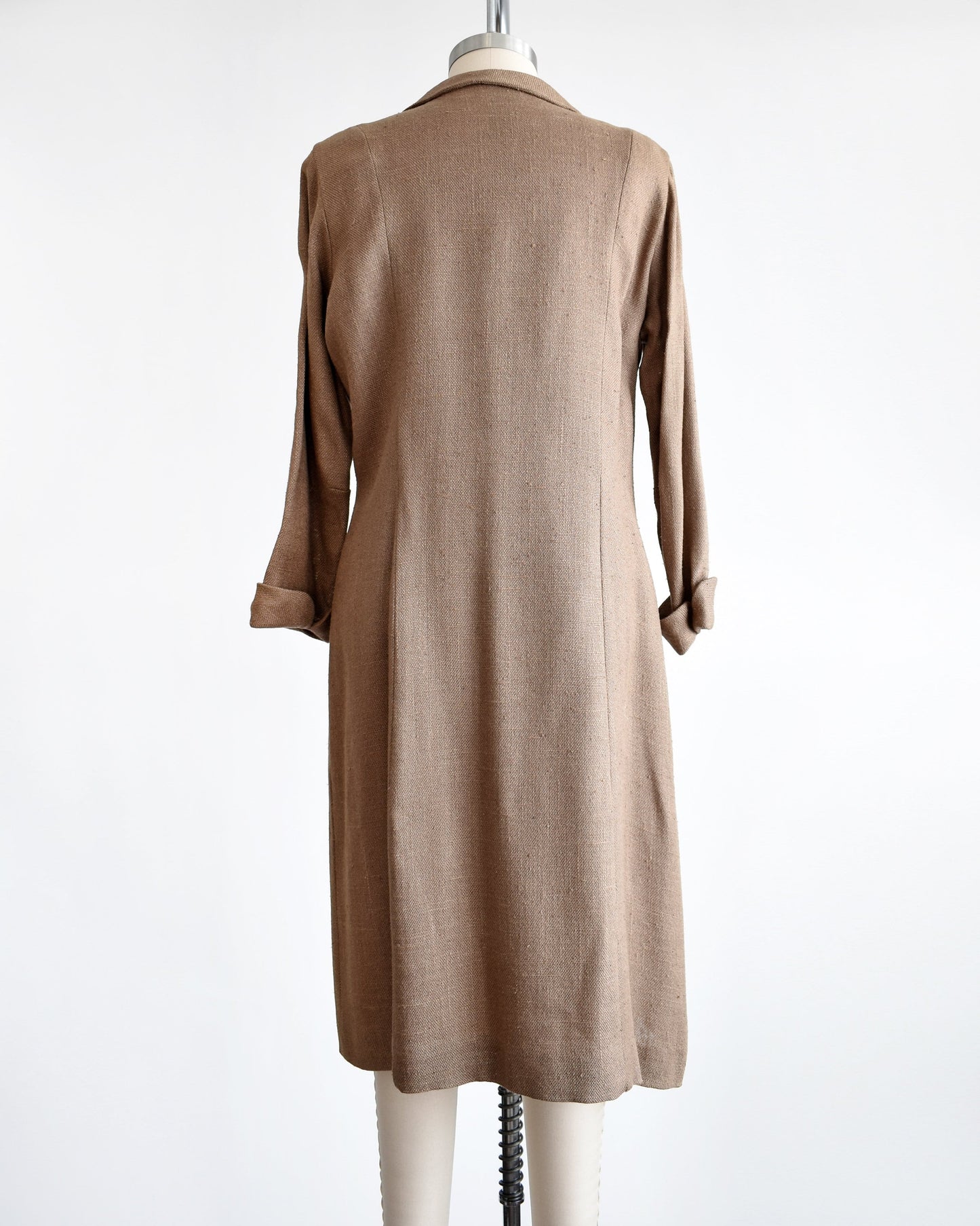 Back view of a vintage late 50s early light brown wool swing coat. The coat has a rounded Peter Pan style collar, four buttons underneath and cuffed long sleeves. The coat is modeled on a dress form.