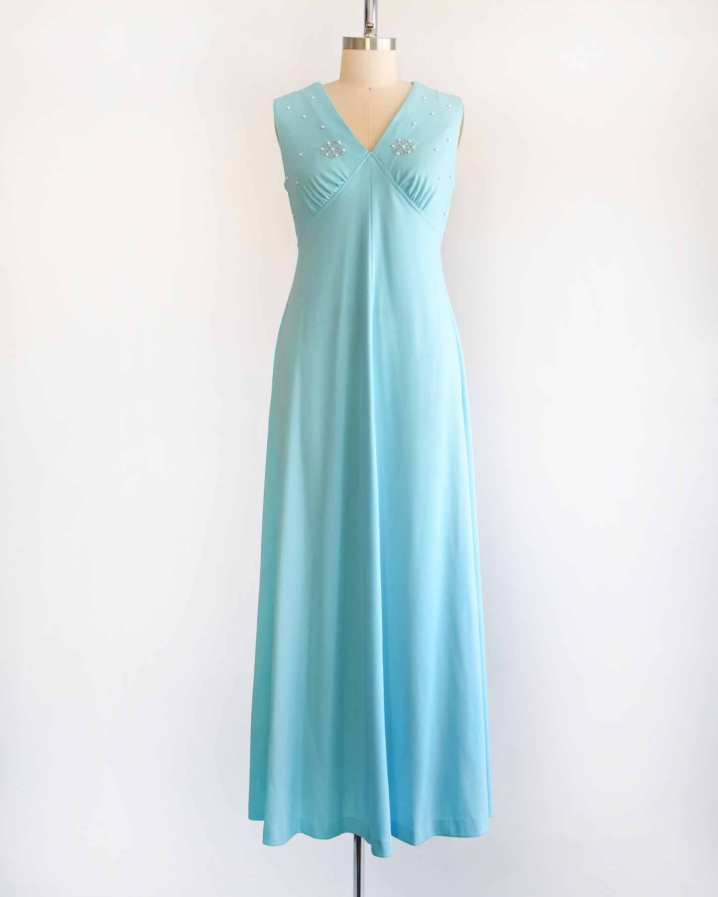 A vintage 70s blue maxi dress with small beads on the bodice. The dress is on a dress form.