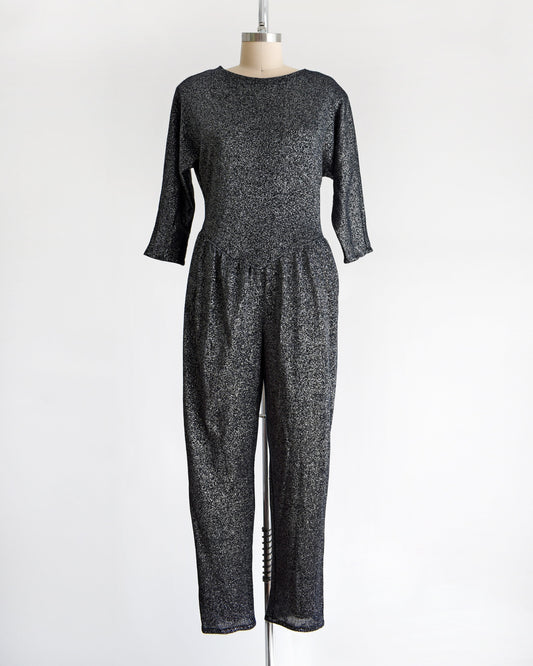 A vintage black and metallic silver jumpsuit. The silver metallic lurex threads are woven throughout, which gives the garment lots of sparkle. The garment is modeled on a dress form.