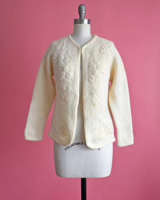 A vintage 60s cream cardigan with matching floral embroidery on the front. The sweater is on a dress form.