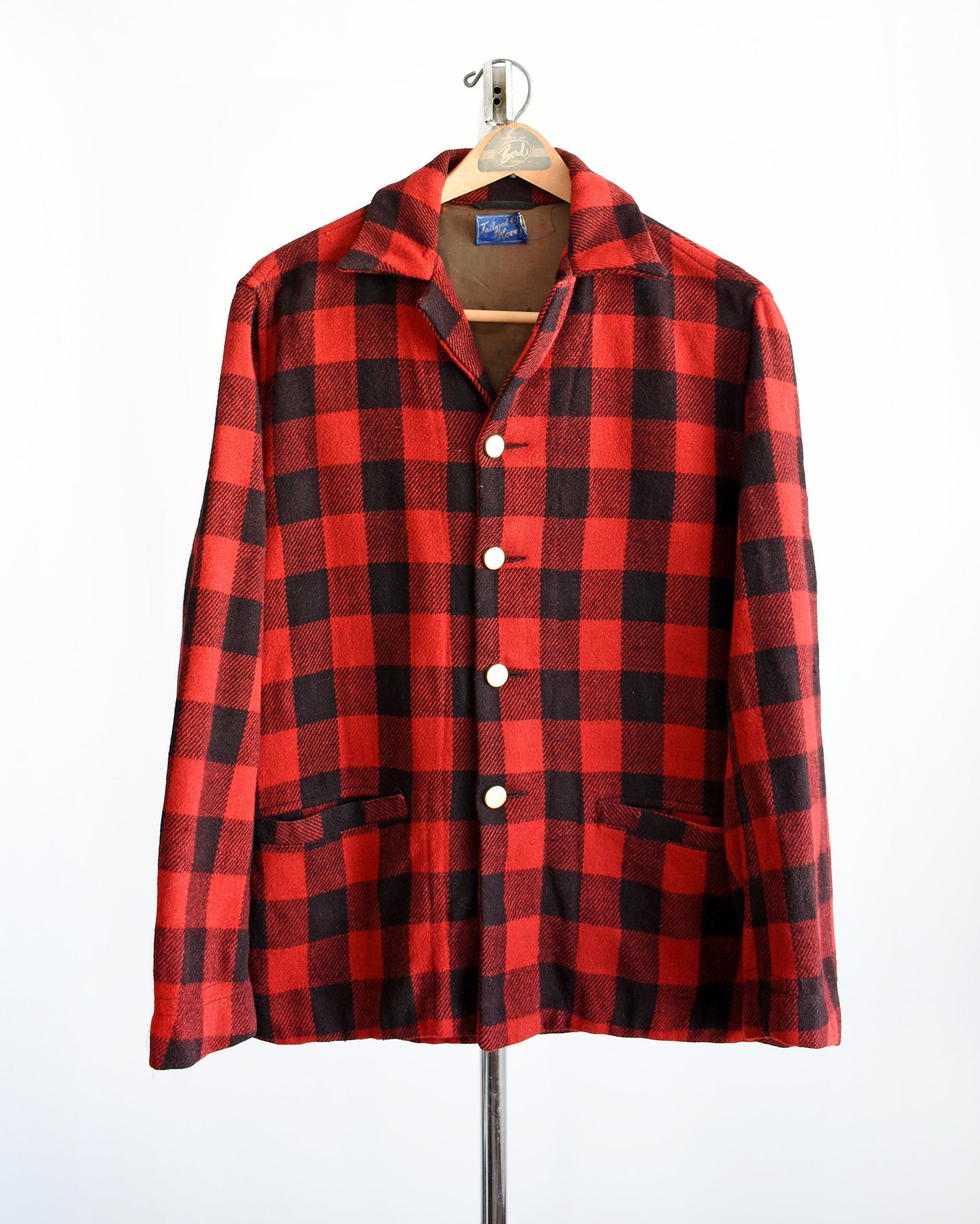 A photo of a vintage 40s red and black plaid jacket with gold buttons down the front. The jacket is modeled on a hanger.