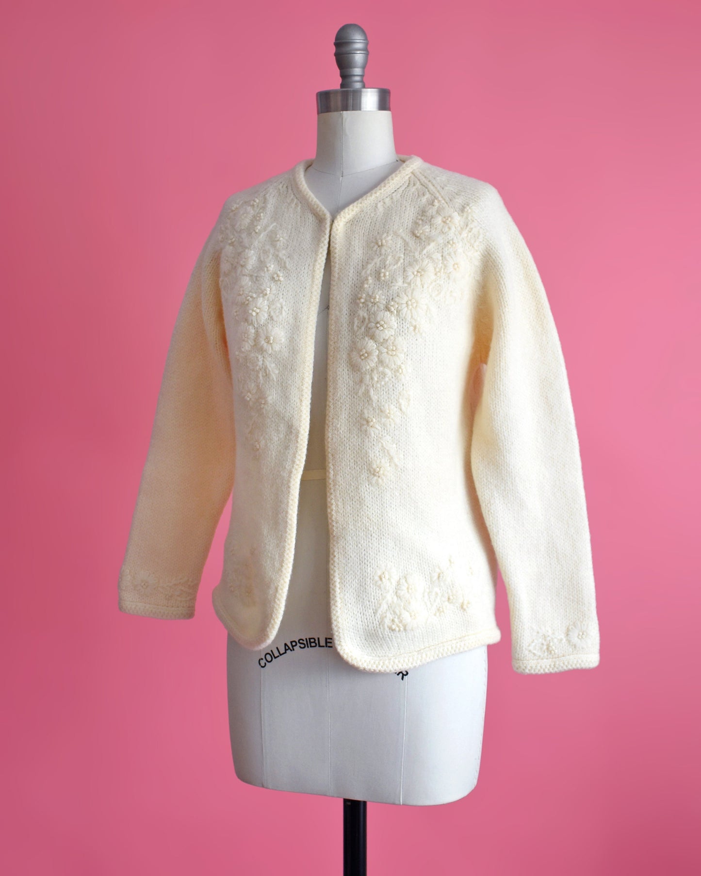 Side front view of a vintage 60s cream cardigan with matching floral embroidery on the front. The sweater is on a dress form.