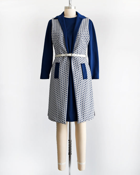 A vintage 60s/70s two piece dress set that features a long sleeve navy dress with a white and navy diamond print long vest. The dress is belted in the photo, but the belt is not included. Dress is modeled on a dress form.