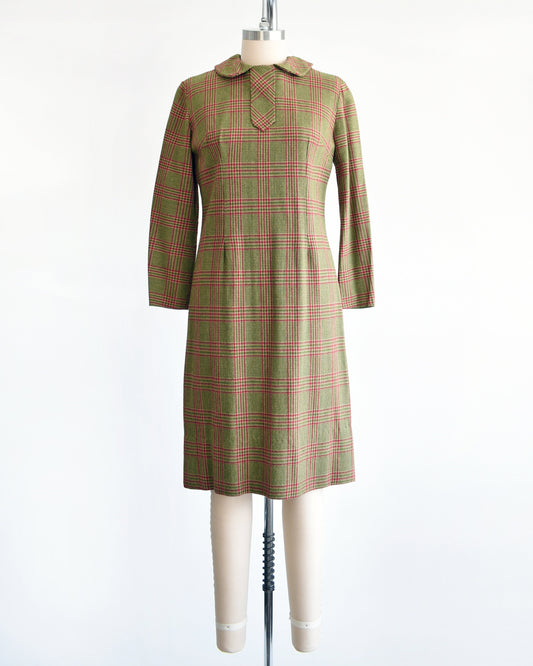 A vintage 60s green and pink plaid wool dress with Peter Pan style collar and long sleeves. The dress is modeled on a dress form.