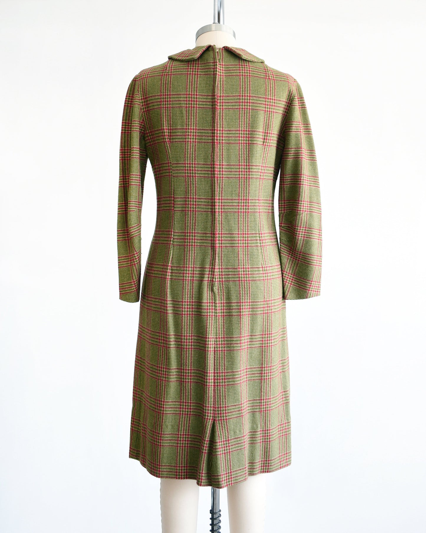 Back view of a vintage 60s green and pink plaid wool dress with Peter Pan style collar and long sleeves. The dress is modeled on a dress form.