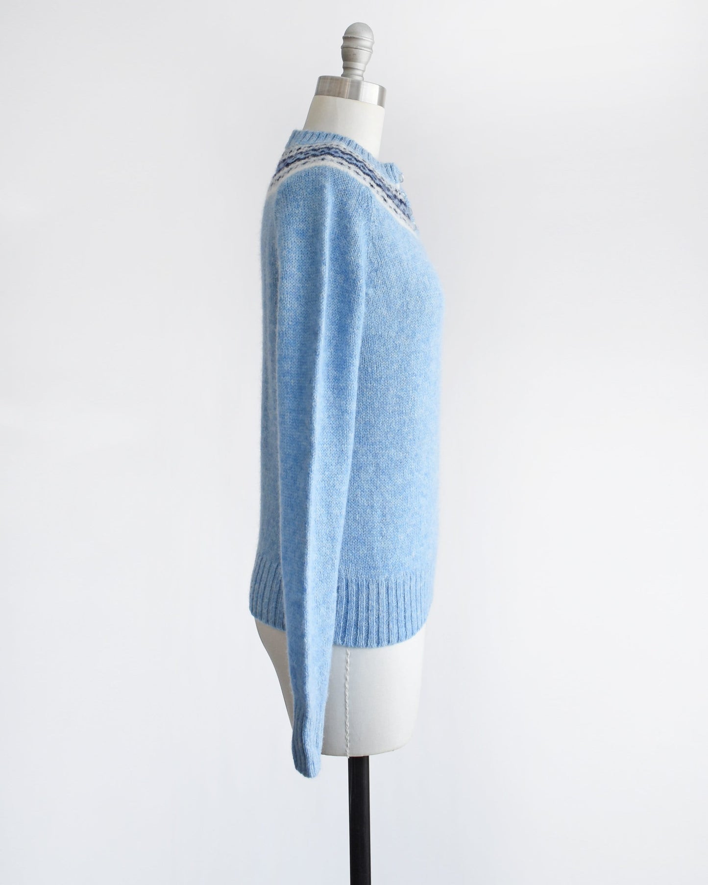 Side view of a vintage 80s blue sweater with a fair isle pattern around the collar. The sweater is modeled on a dress form.vintage 80s blue sweater with a fair isle pattern around the collar. The sweater is modeled on a dress form.