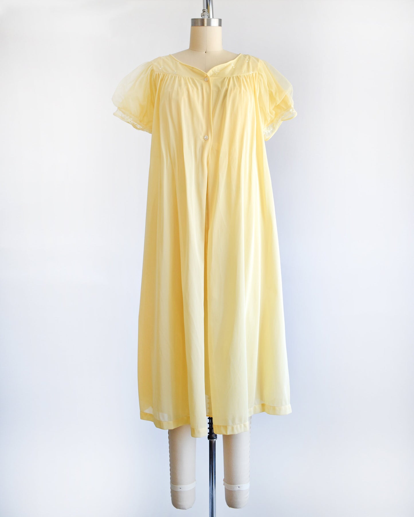A vintage 60s yellow peignoir set that has a yellow robe with puff sleeves. The set is modeled on a dress form.