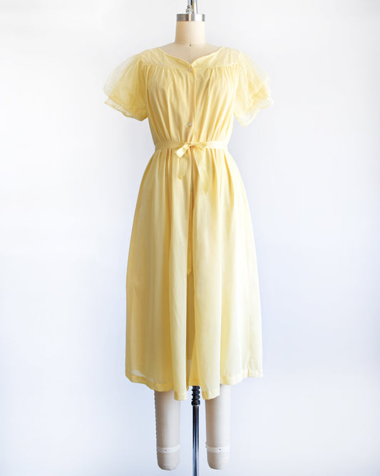 A vintage 60s yellow peignoir set that has a yellow robe with puff sleeves and a ribbon at the waist. The set is modeled on a dress form.
