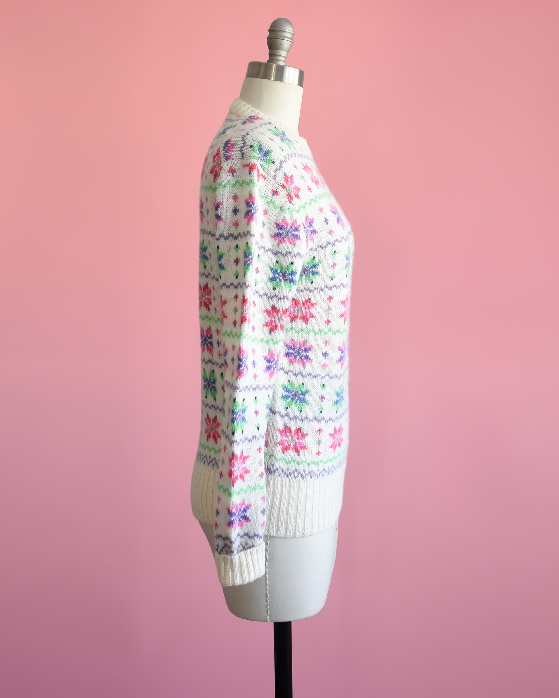 Side view of a vintage 80s white wool sweater with a green, pink, purple, and blue snowflake pattern on a dress form.