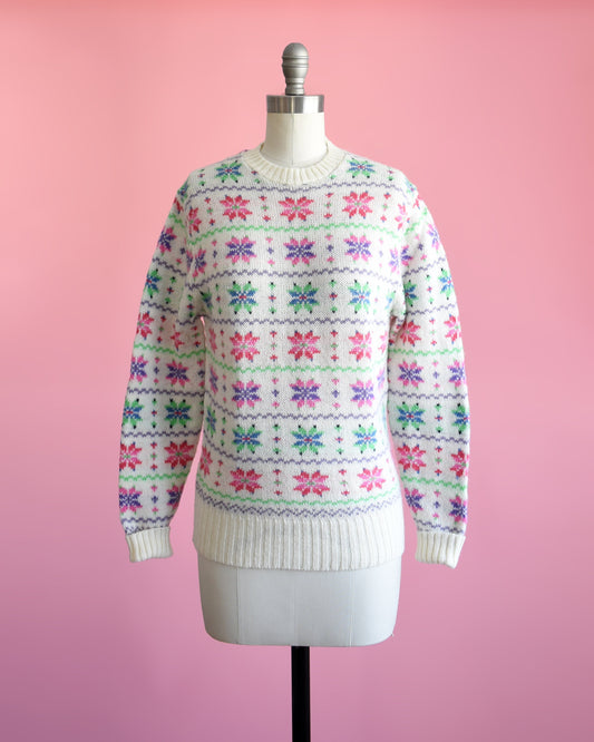 A vintage 80s white wool sweater with a green, pink, purple, and blue snowflake pattern on a dress form.