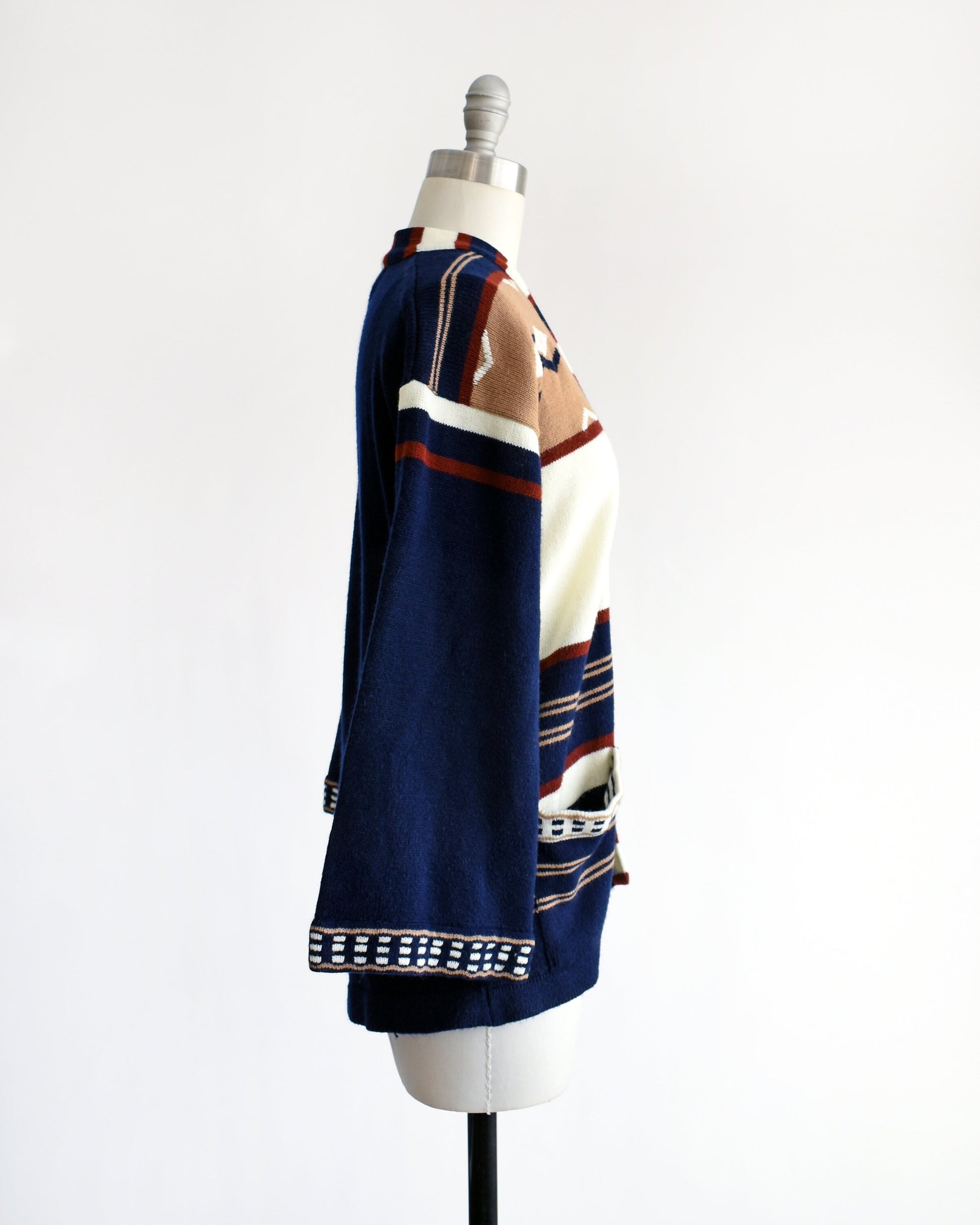 Side view of a vintage 70s navy blue, tan, reddish brown, and white striped bell sleeve open cardigan on a dress form.