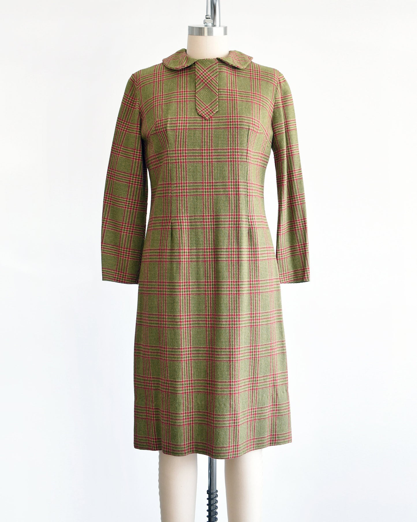 A vintage 60s green and pink plaid wool dress with Peter Pan style collar and long sleeves. The dress is modeled on a dress form.
