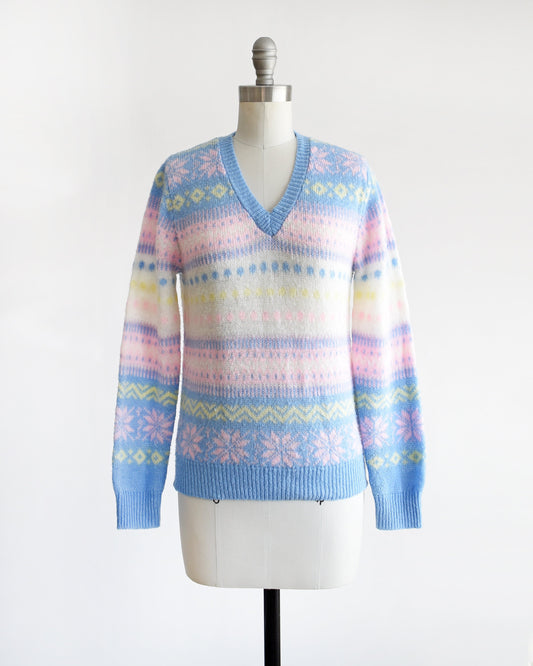 A vintage 80s pastel striped sweater that is blue, pink, yellow, and white, and at has a snowflake and geometric stripe print on a dress form.
